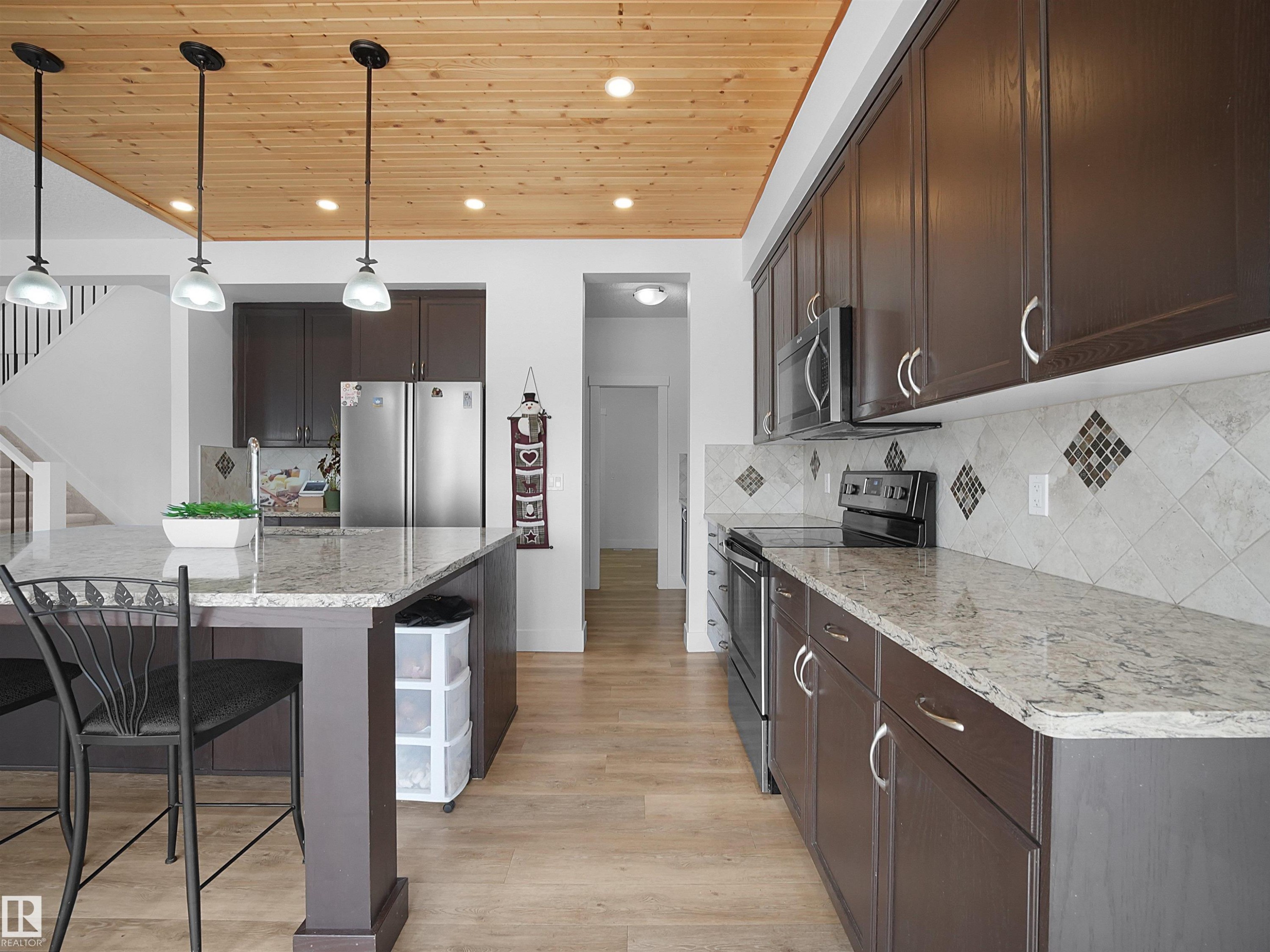 Kitchen featuring a wood plank ceiling with recessed lighting, pendant lights over the island, dark wood cabinetry, granite countertops, and a tiled backsplash with decorative accents - 4231 Charles Close, Edmonton, AB - Indoor Photo Showing Kitchen With Stainless Steel Kitchen With Upgraded Kitchen