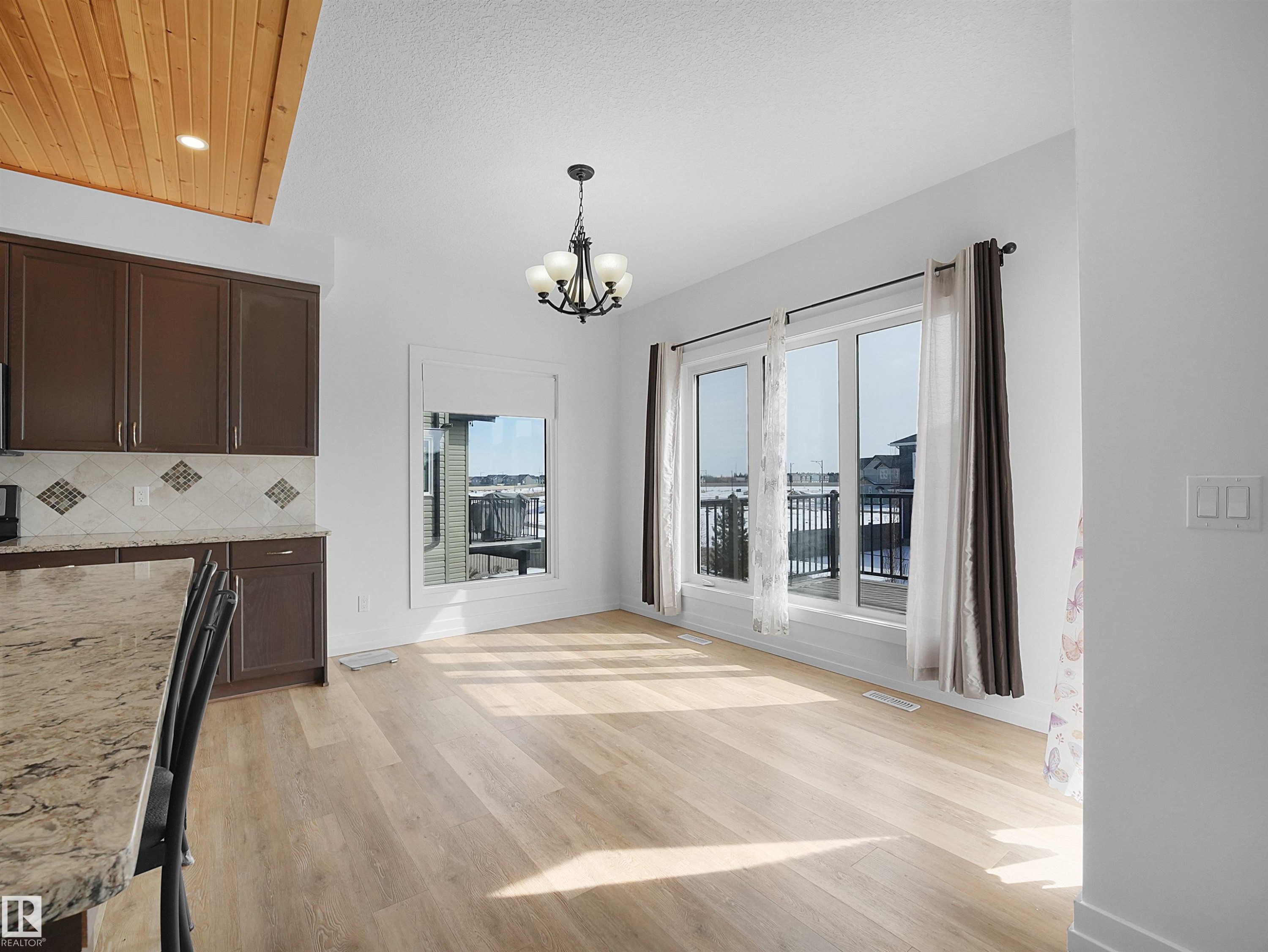 This bright and open room features light-toned flooring, a chandelier, and large windows with a view of a deck and railing - 4231 Charles Close, Edmonton, AB - Indoor Photo Showing Kitchen