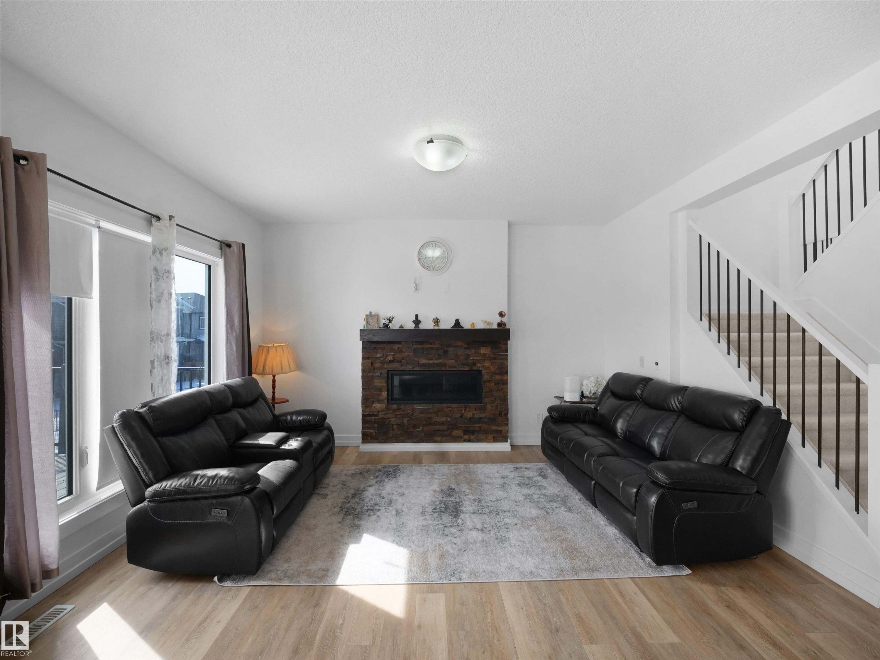 Living space featuring light-toned flooring, a stone-clad fireplace, and a staircase with white risers and dark balusters - 4231 Charles Close, Edmonton, AB - Indoor Photo Showing Living Room With Fireplace