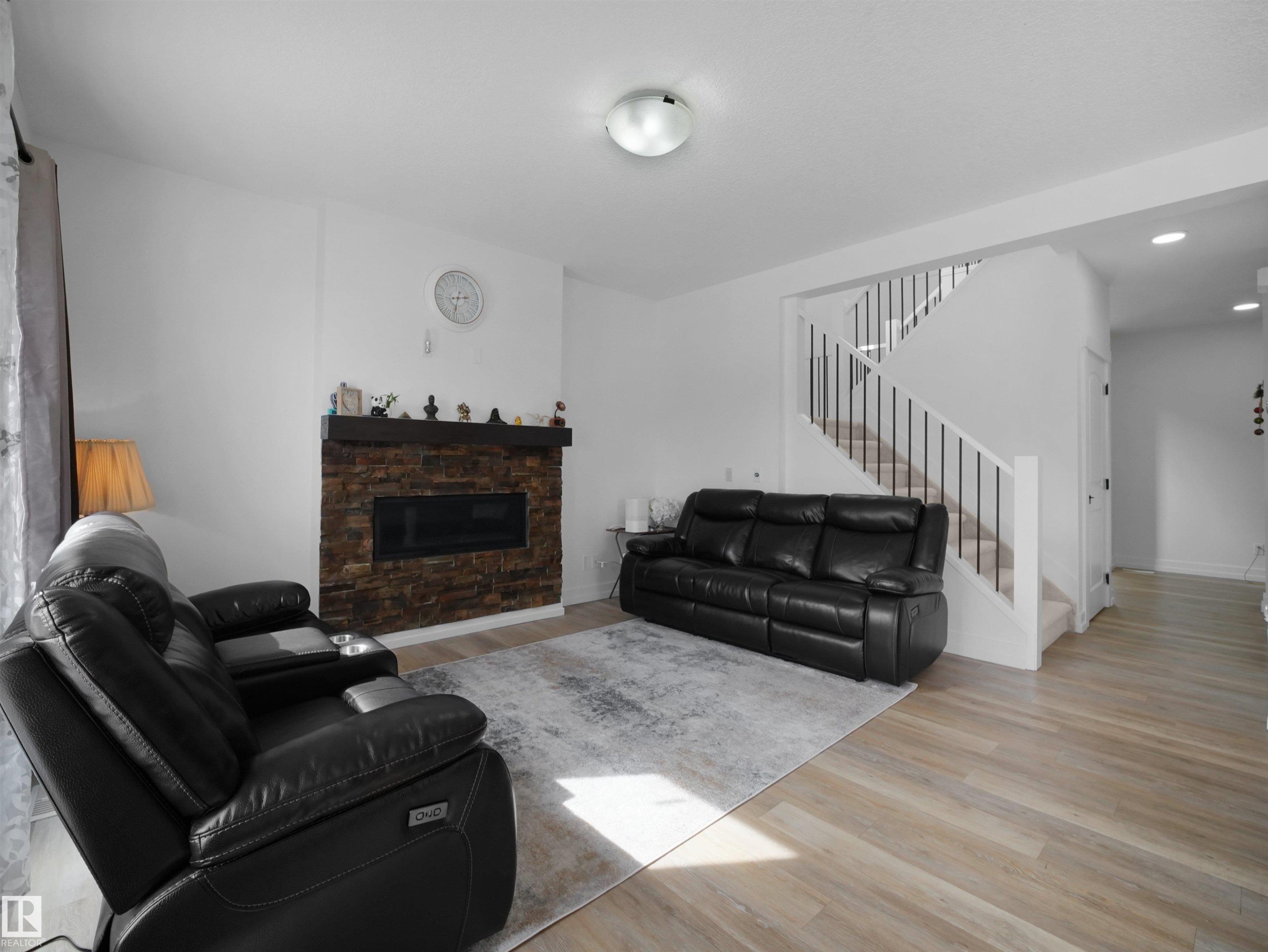 Inviting living space featuring light-colored flooring, a fireplace with a stone surround, and a staircase with white risers and dark banisters - 4231 Charles Close, Edmonton, AB - Indoor Photo Showing Living Room With Fireplace