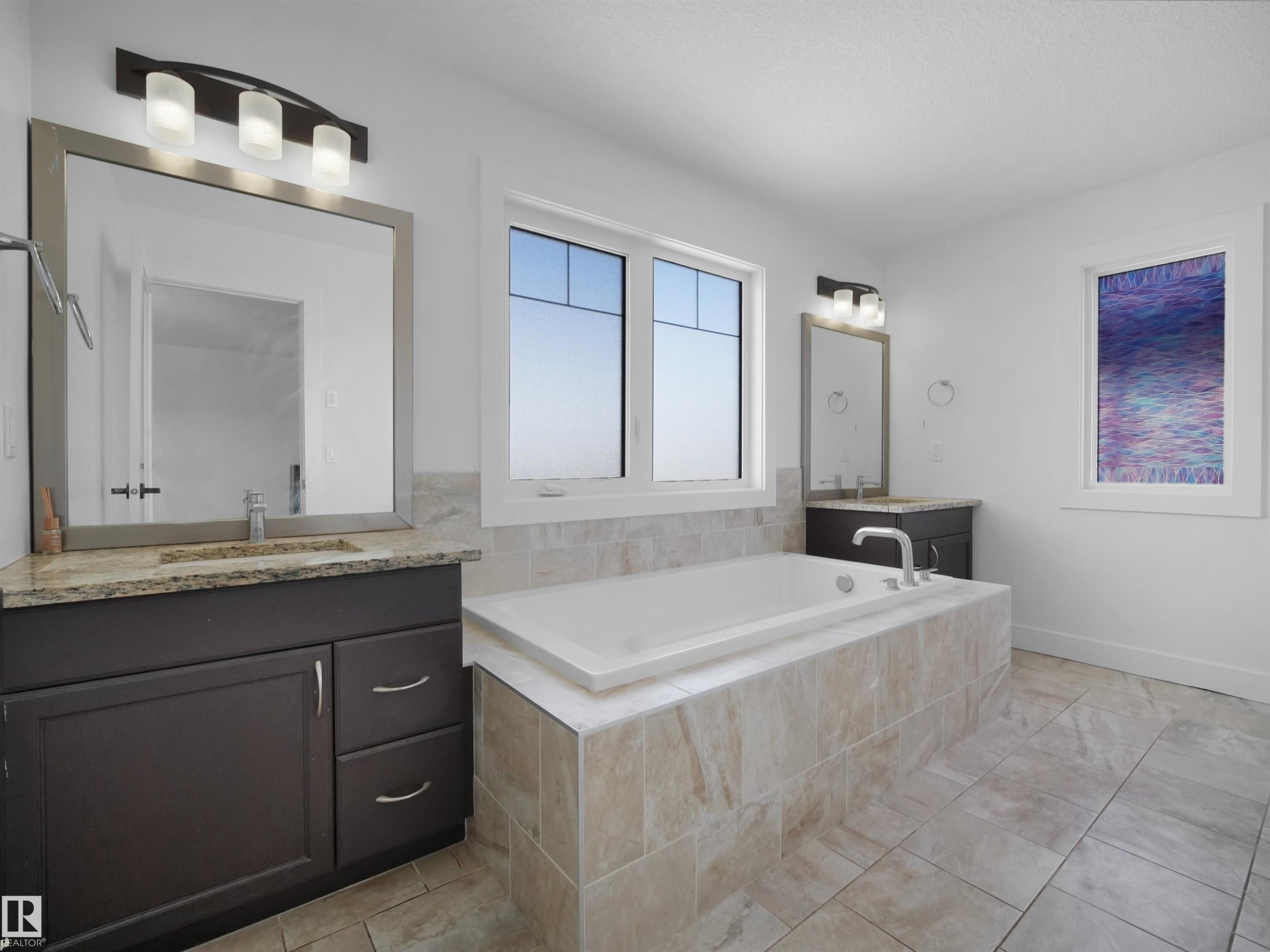 The bathroom features a built-in tub with tile surround, two windows, and two separate vanities with mirrors and overhead lighting - 4231 Charles Close, Edmonton, AB - Indoor Photo Showing Bathroom