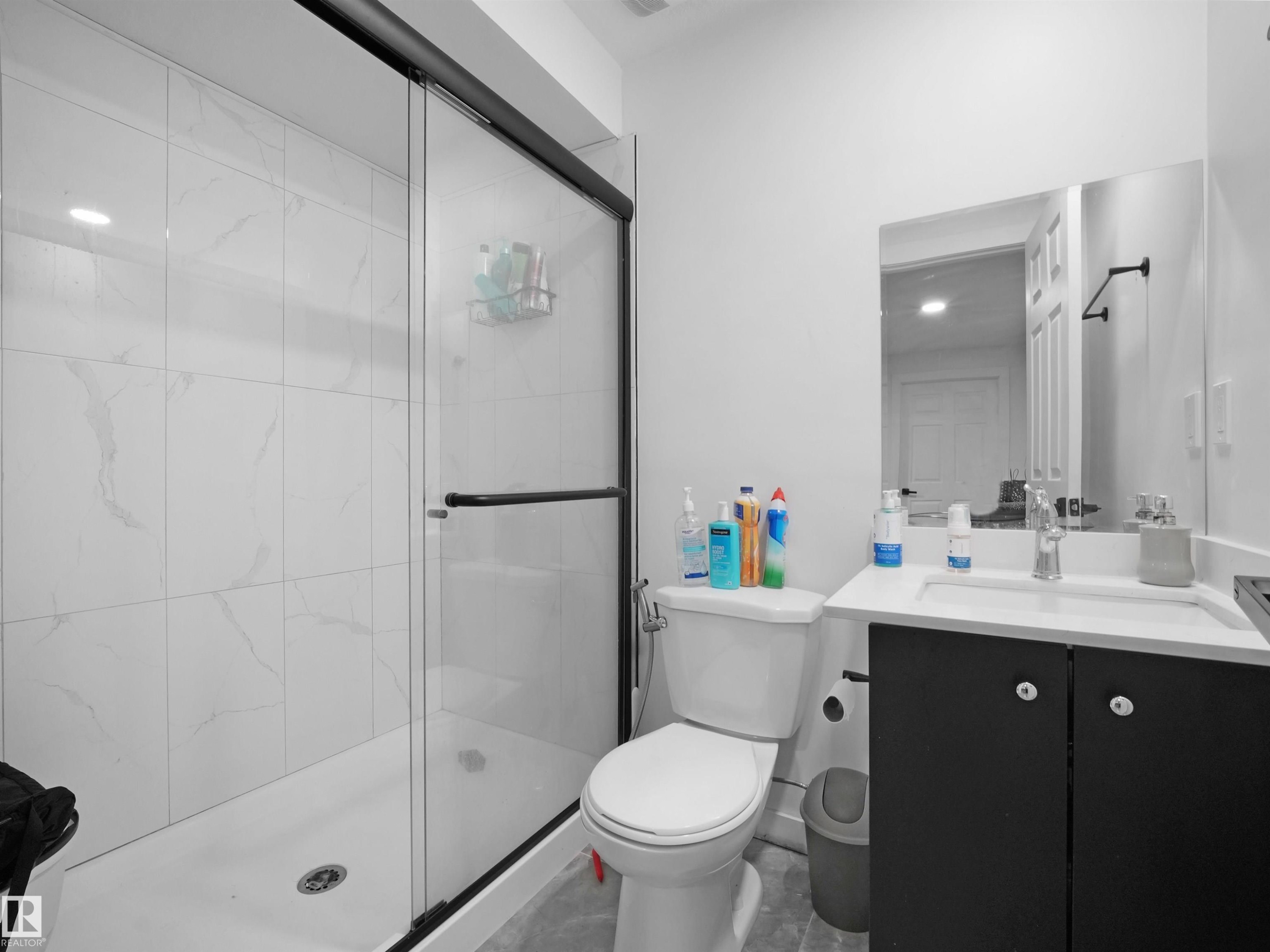 Bathroom featuring a glass-enclosed shower with white tiled walls, a white vanity with a dark cabinet, and a wall-mounted mirror - 4231 Charles Close, Edmonton, AB - Indoor Photo Showing Bathroom