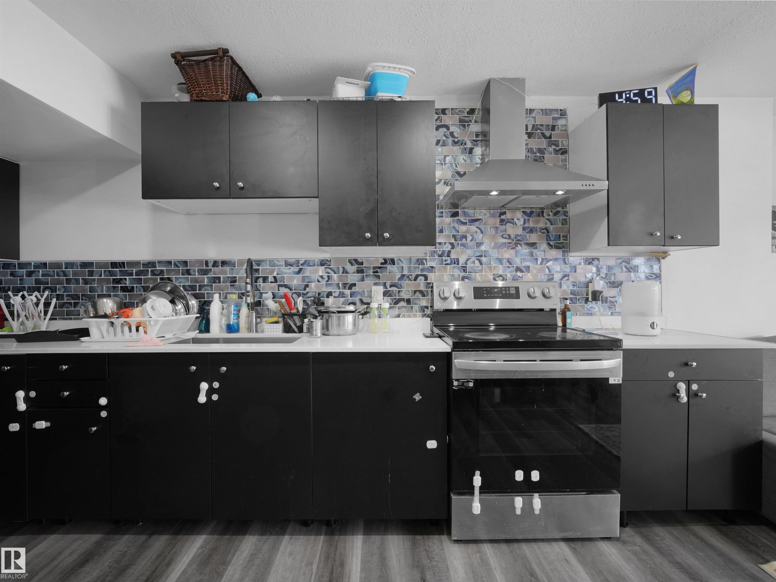 The kitchen features dark cabinetry, white countertops, a mosaic tile backsplash, and stainless steel appliances including a range and range hood - 4231 Charles Close, Edmonton, AB - Indoor Photo Showing Kitchen