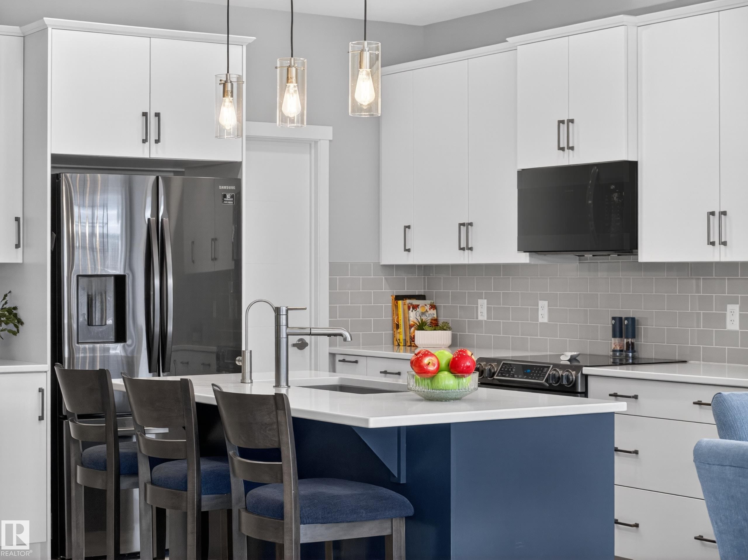 Modern kitchen featuring a blue island with seating, white shaker cabinetry, stainless steel refrigerator, black range, and an over-the-range microwave - 323 Balsam Link, Leduc, AB - Indoor Photo Showing Kitchen With Upgraded Kitchen