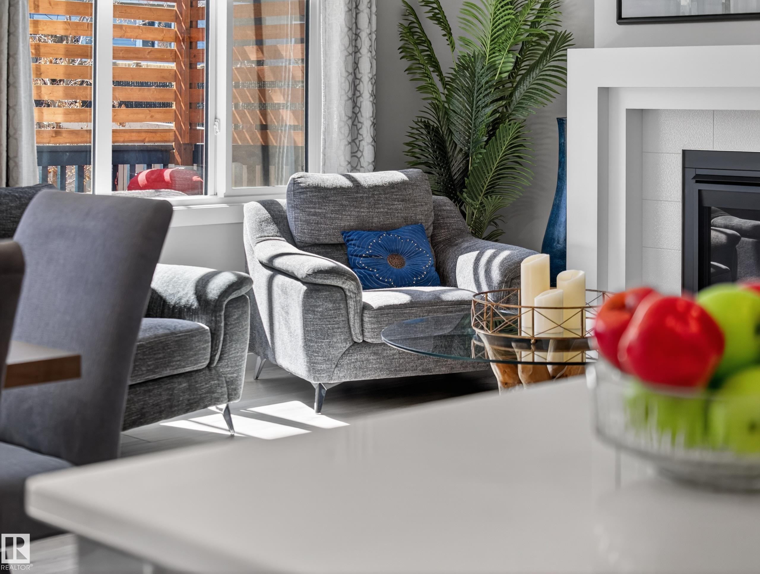 Living area featuring light wood-finish flooring, a contemporary fireplace with a white surround, and large windows with horizontal wood slat privacy screening - 323 Balsam Link, Leduc, AB - Photo Showing Living Room