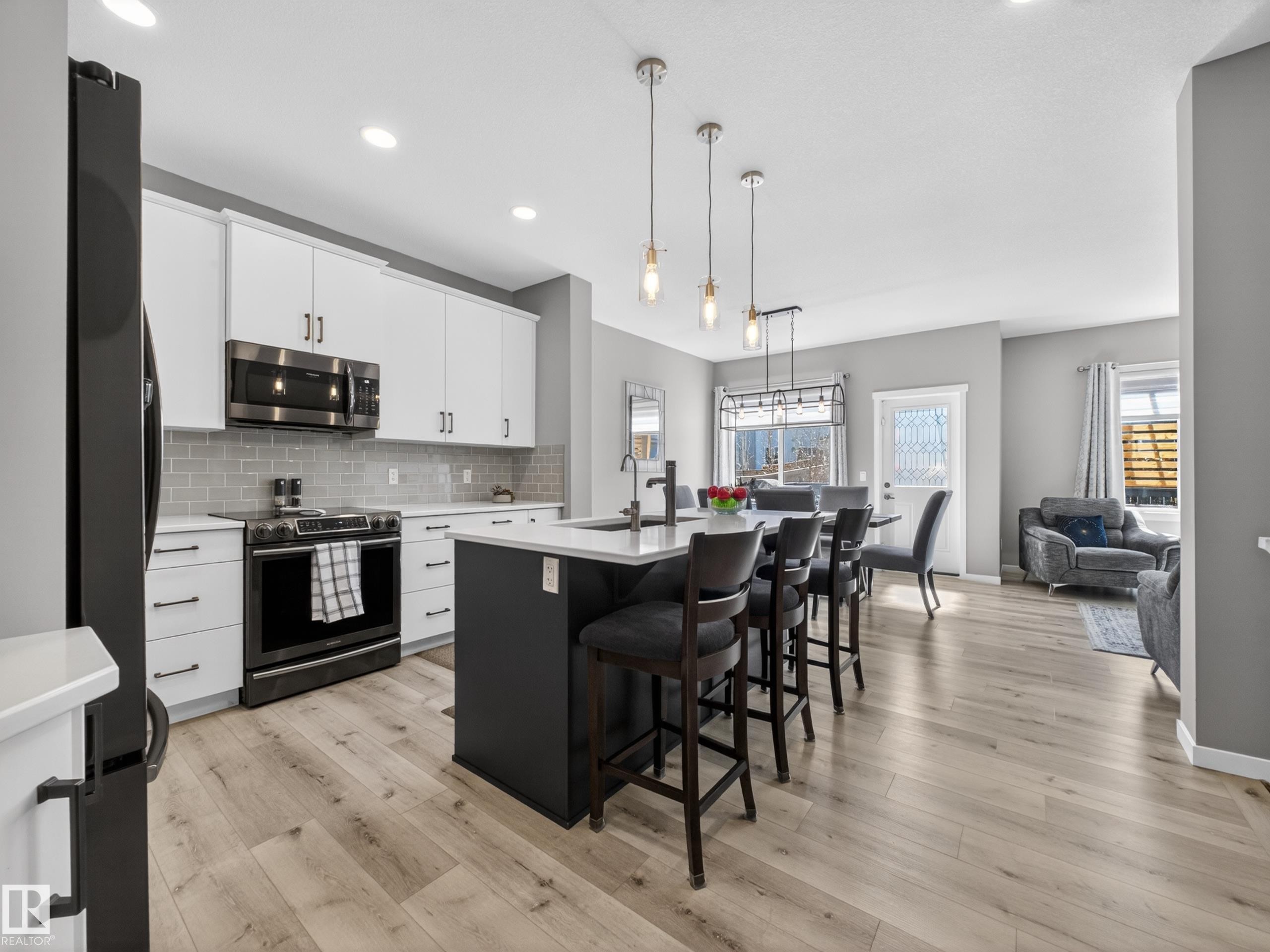 Contemporary kitchen featuring white cabinetry, subway tile backsplash, stainless steel appliances, and a central island with bar seating - 323 Balsam Link, Leduc, AB - Indoor Photo Showing Other Room