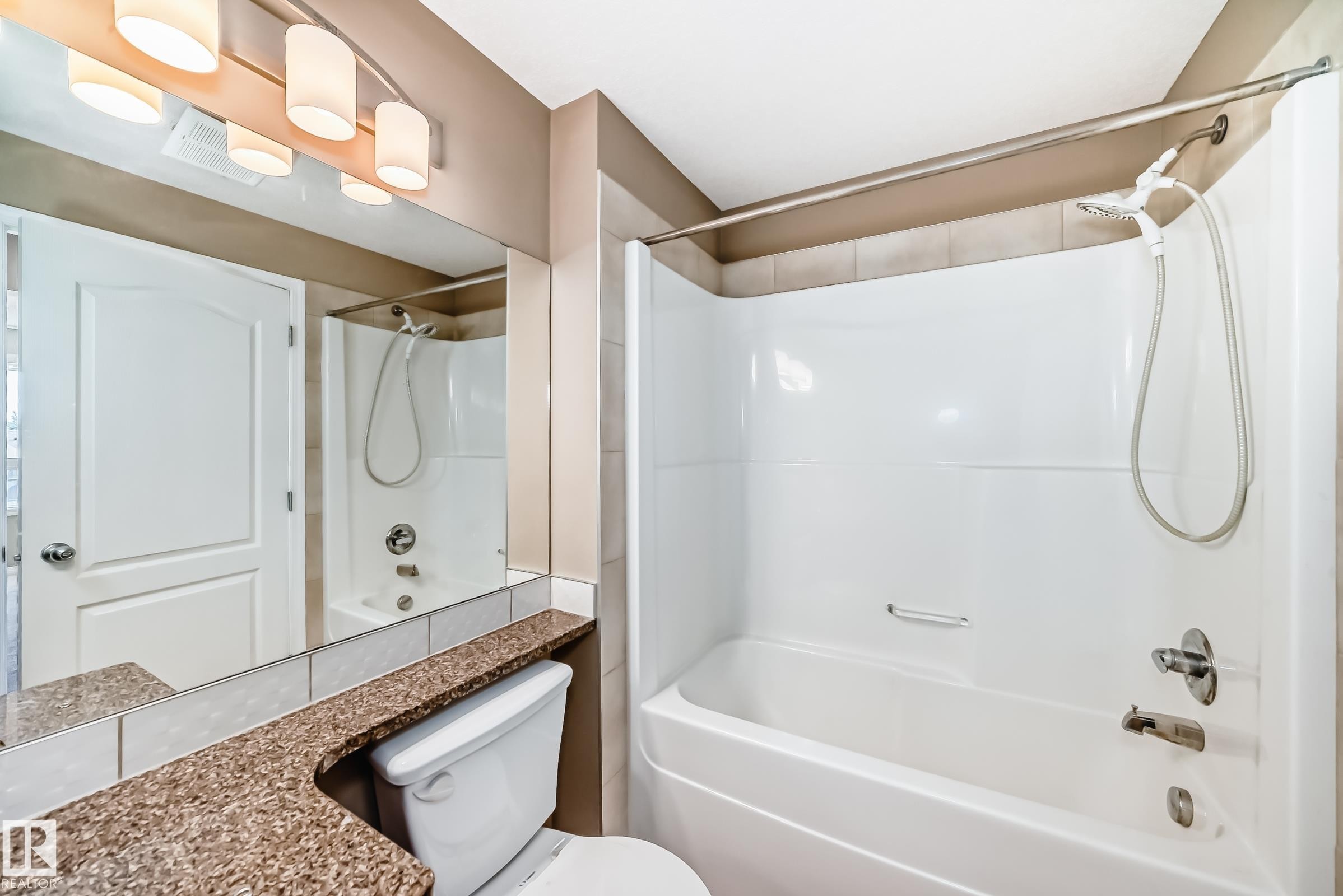Bathroom featuring a white tub-shower combination with a handheld showerhead, a large vanity mirror, a vanity countertop with a speckled finish, and contemporary light fixtures - 344 1520 Hammond Gate Gate, Edmonton, AB - Indoor Photo Showing Bathroom