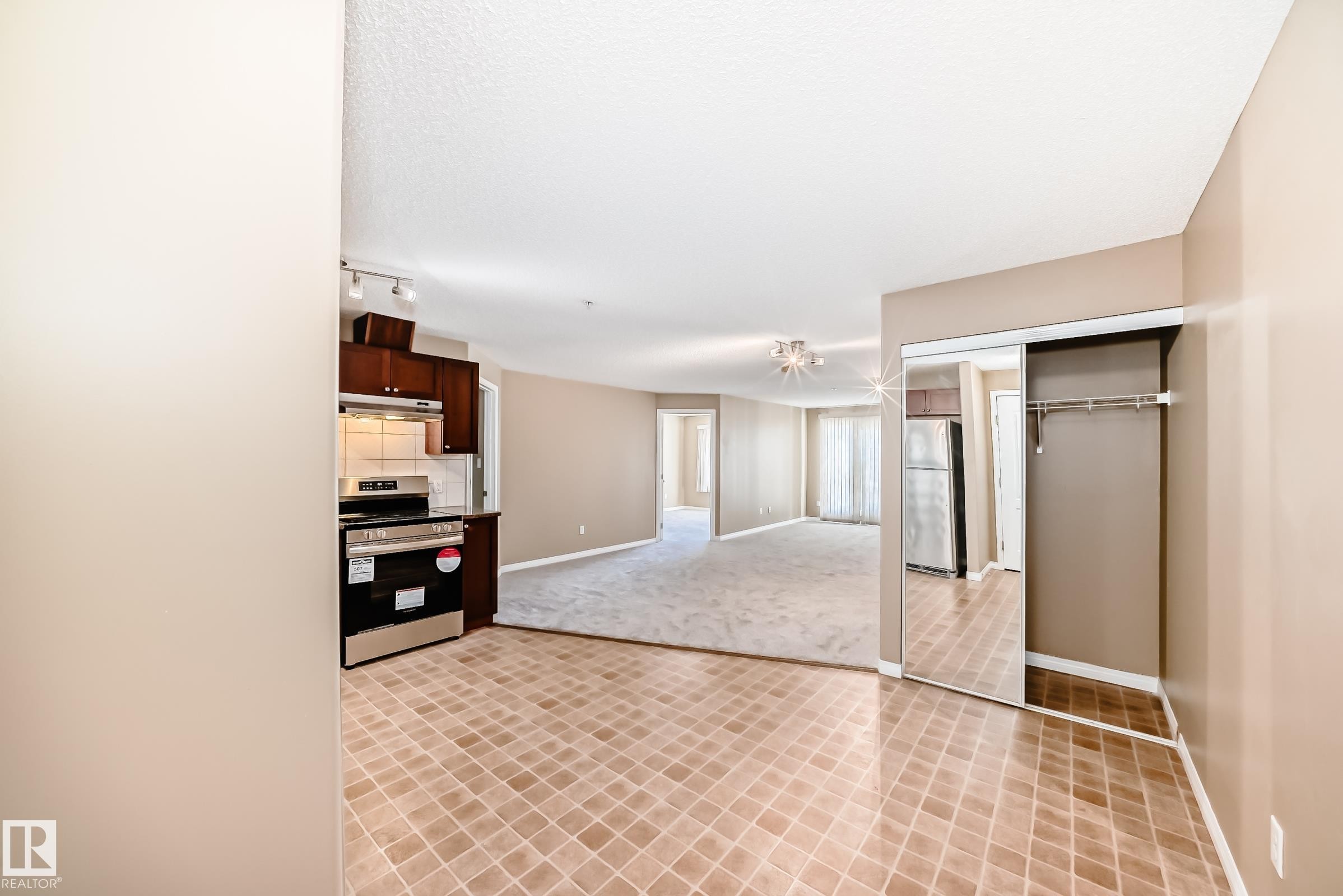 Kitchen area featuring dark wood-finish cabinetry, stainless steel range, and tile backsplash - 344 1520 Hammond Gate Gate, Edmonton, AB - Indoor Photo Showing Other Room