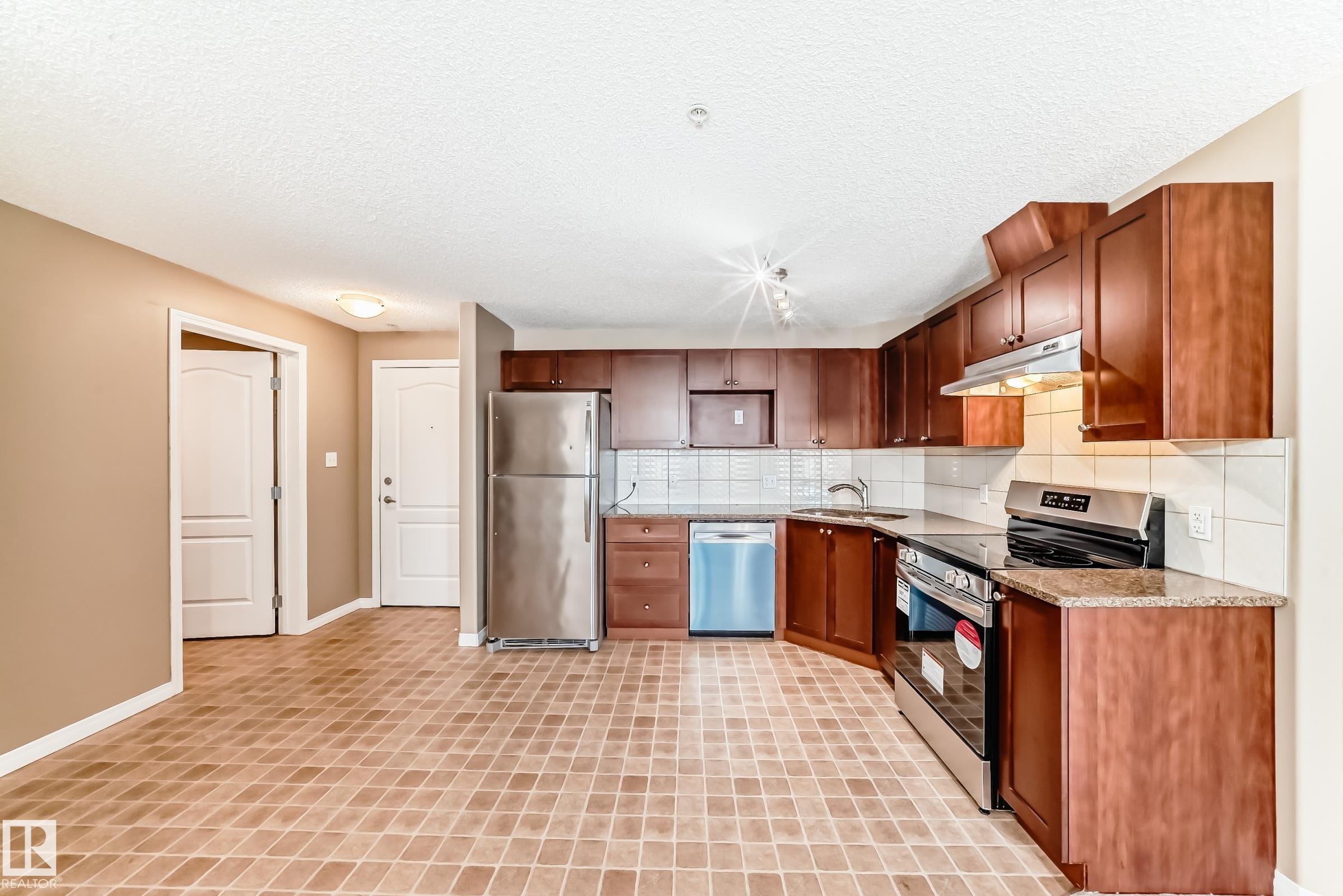 Open-concept kitchen featuring wood-finish cabinetry, stainless steel appliances, granite-style countertops, and a subway tile backsplash - 344 1520 Hammond Gate Gate, Edmonton, AB - Indoor Photo Showing Kitchen