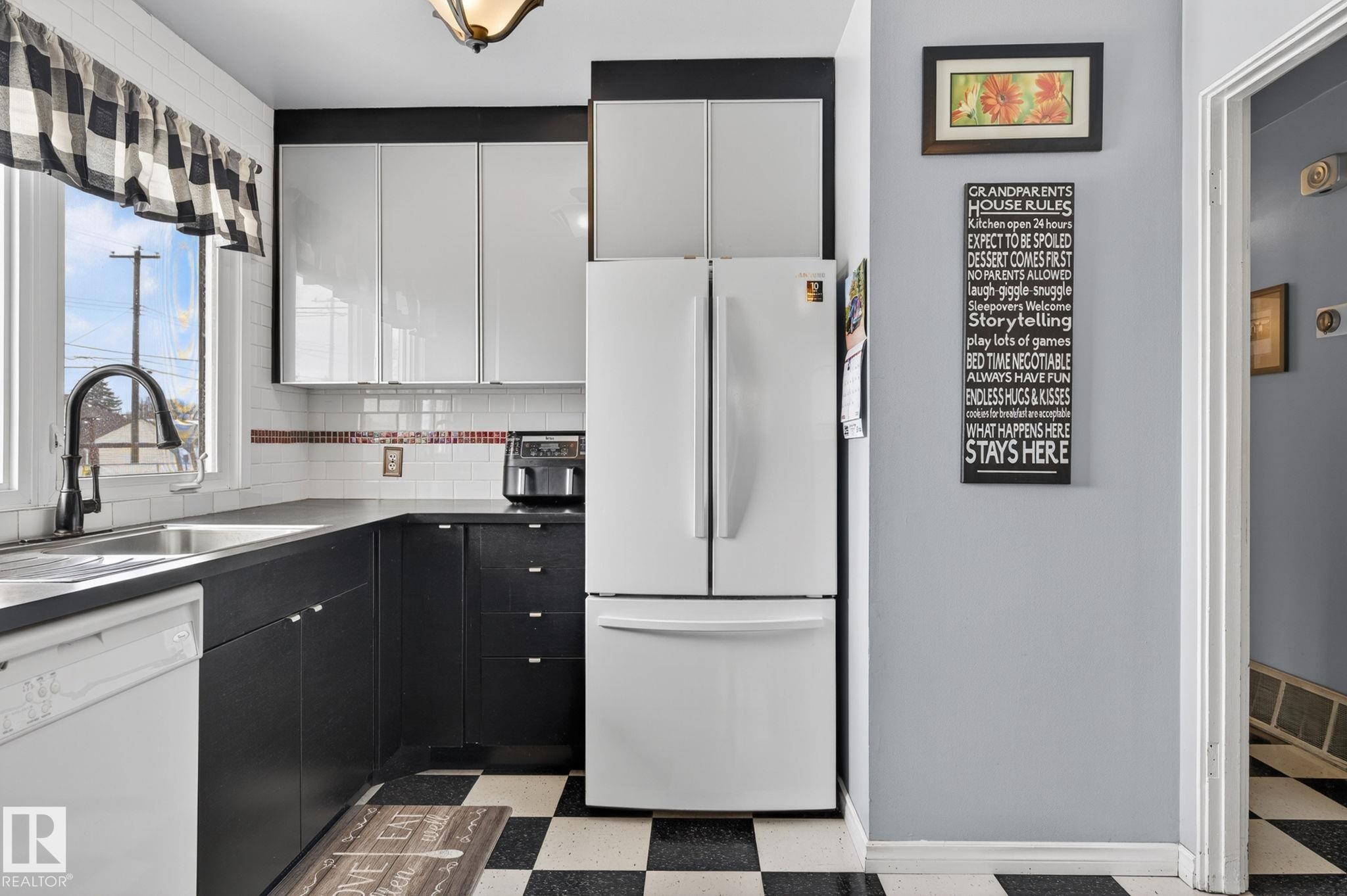 Kitchen featuring black and white cabinetry, a black faucet, a large window, white subway tile backsplash, and checkerboard floor tiling - 9112 130 Avenue, Edmonton, AB - Indoor Photo Showing Kitchen