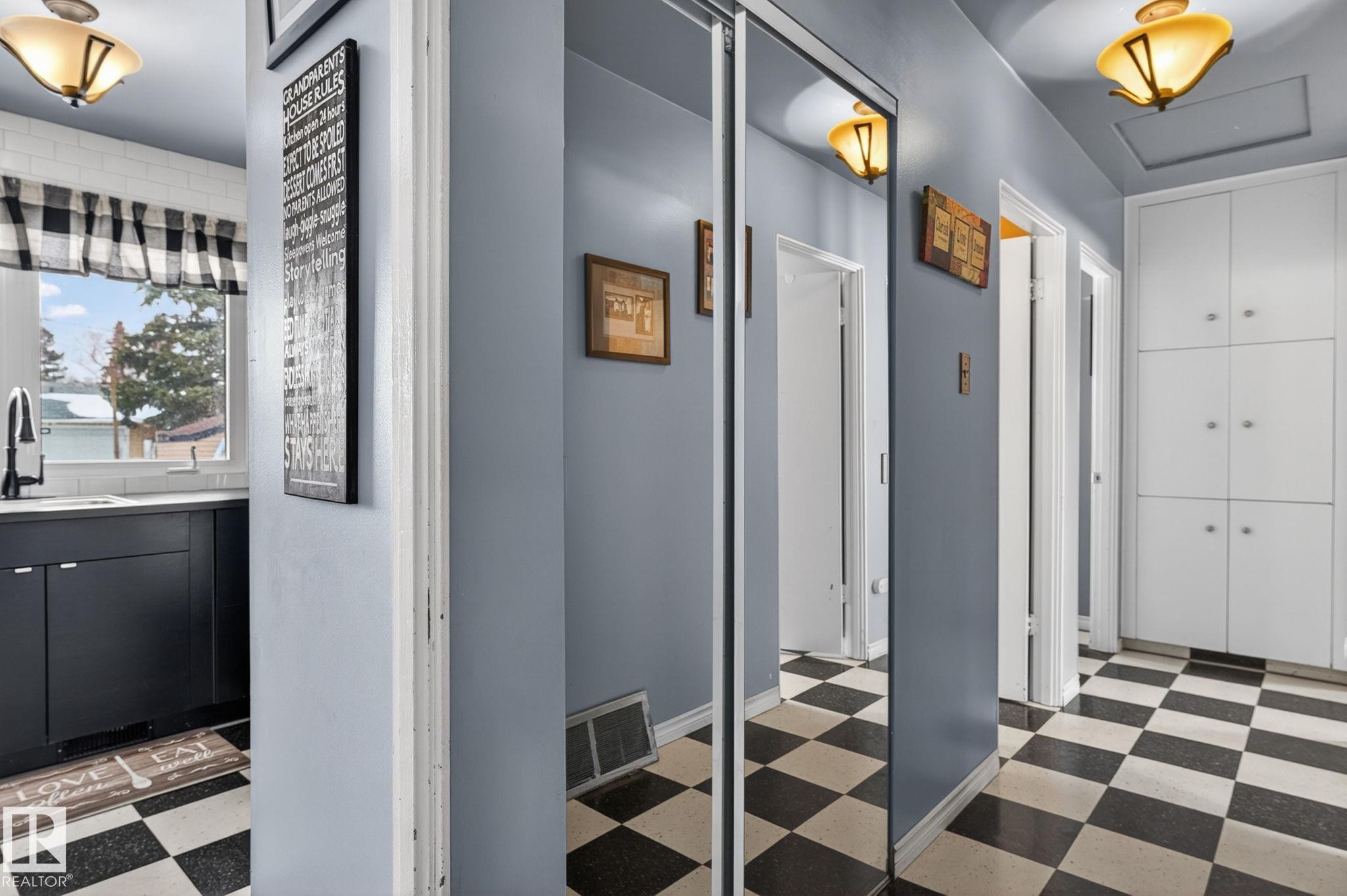 Hallway featuring checkerboard flooring, a wall of built-in white cabinetry with silver hardware, and a mirrored closet - 9112 130 Avenue, Edmonton, AB - Indoor Photo Showing Other Room