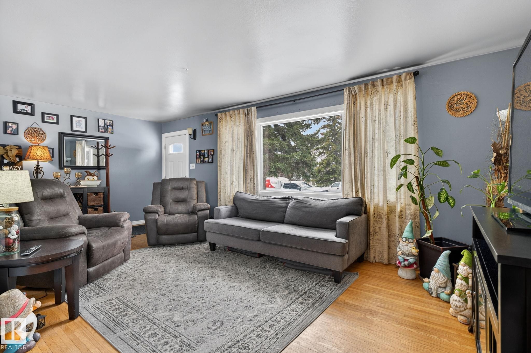 Bright living area featuring wood-finish flooring, a large picture window, and a white paneled entrance door - 9112 130 Avenue, Edmonton, AB - Indoor Photo Showing Living Room