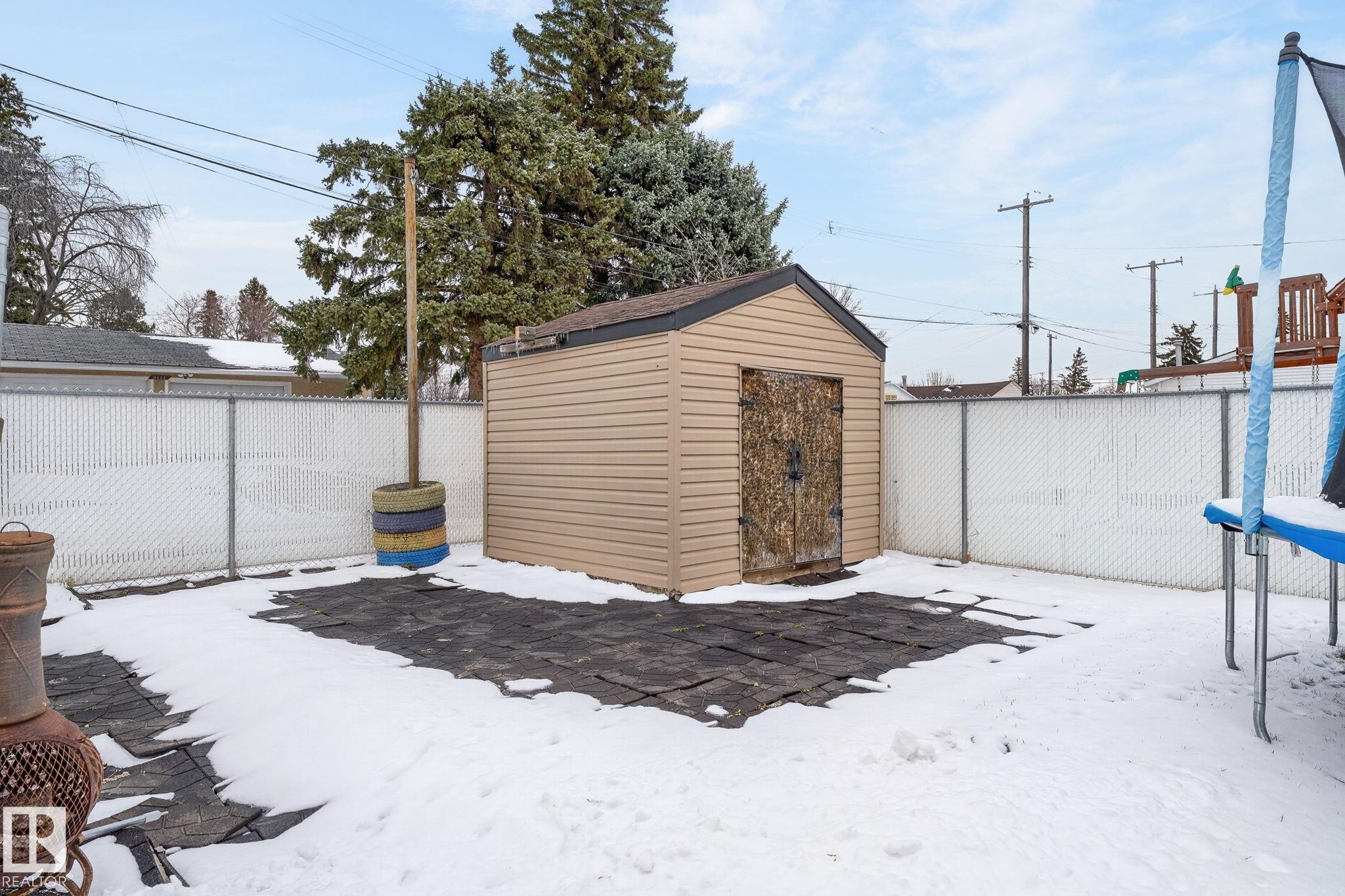 Backyard featuring a tan vinyl-sided storage shed with a dark brown shingled roof, secured by a surrounding chain-link fence - 9112 130 Avenue, Edmonton, AB - Outdoor