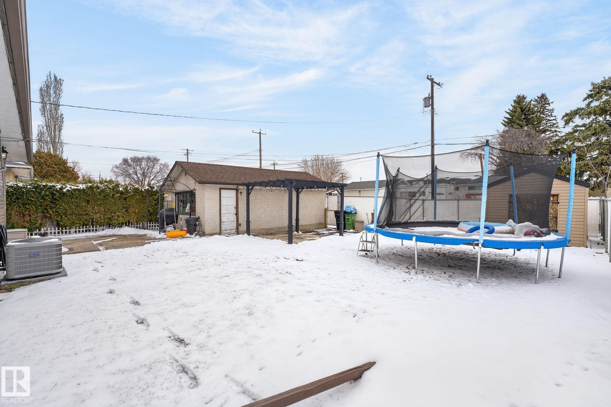 Expansive backyard featuring a concrete patio, a detached garage with an attached pergola, a privacy fence with established hedges, and a secondary storage shed - 9112 130 Avenue, Edmonton, AB - Outdoor