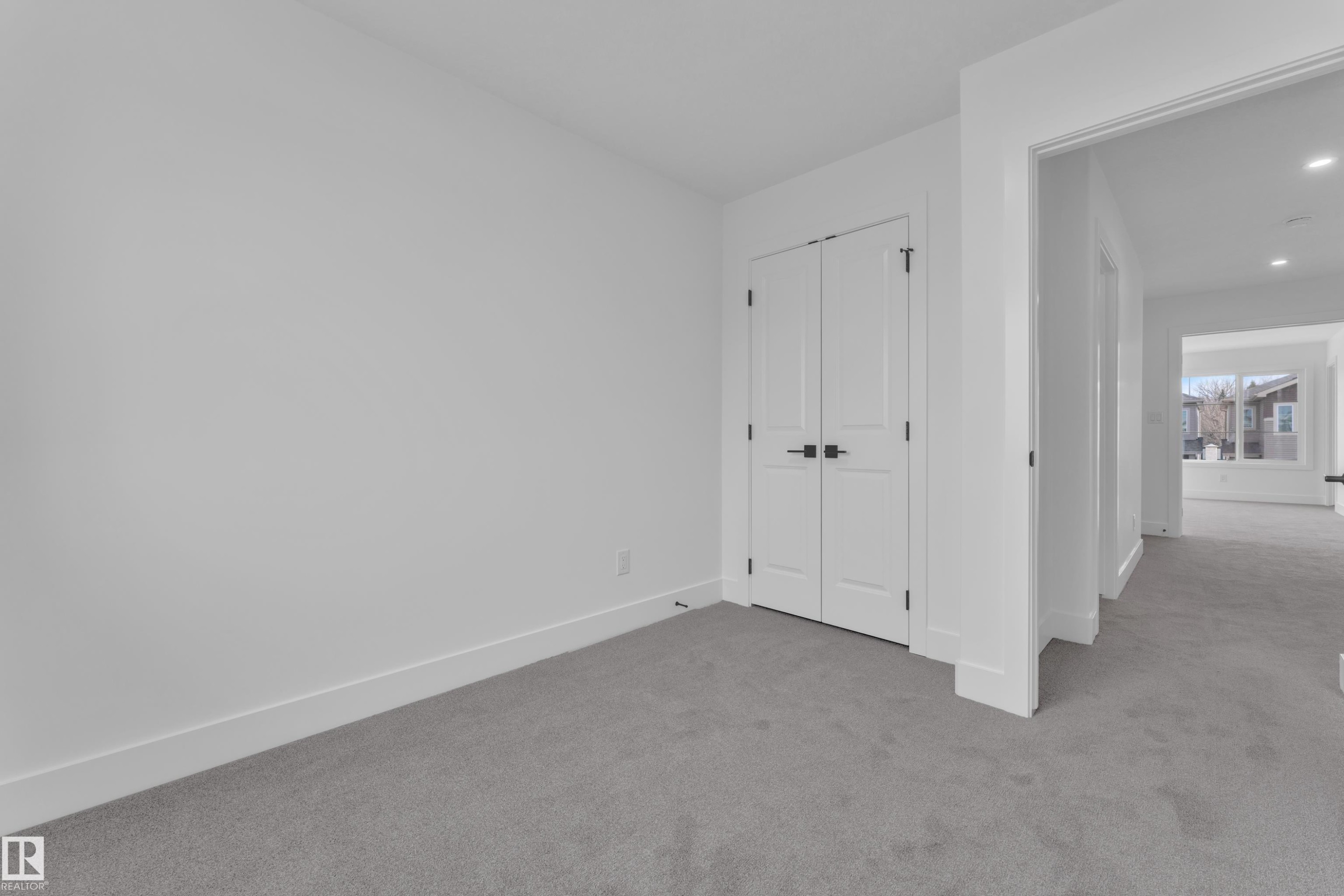 Spacious room featuring light gray carpeting, white walls, white baseboards, and a double-door closet with black hardware - 285 Munn Way, Leduc, AB - Indoor Photo Showing Other Room