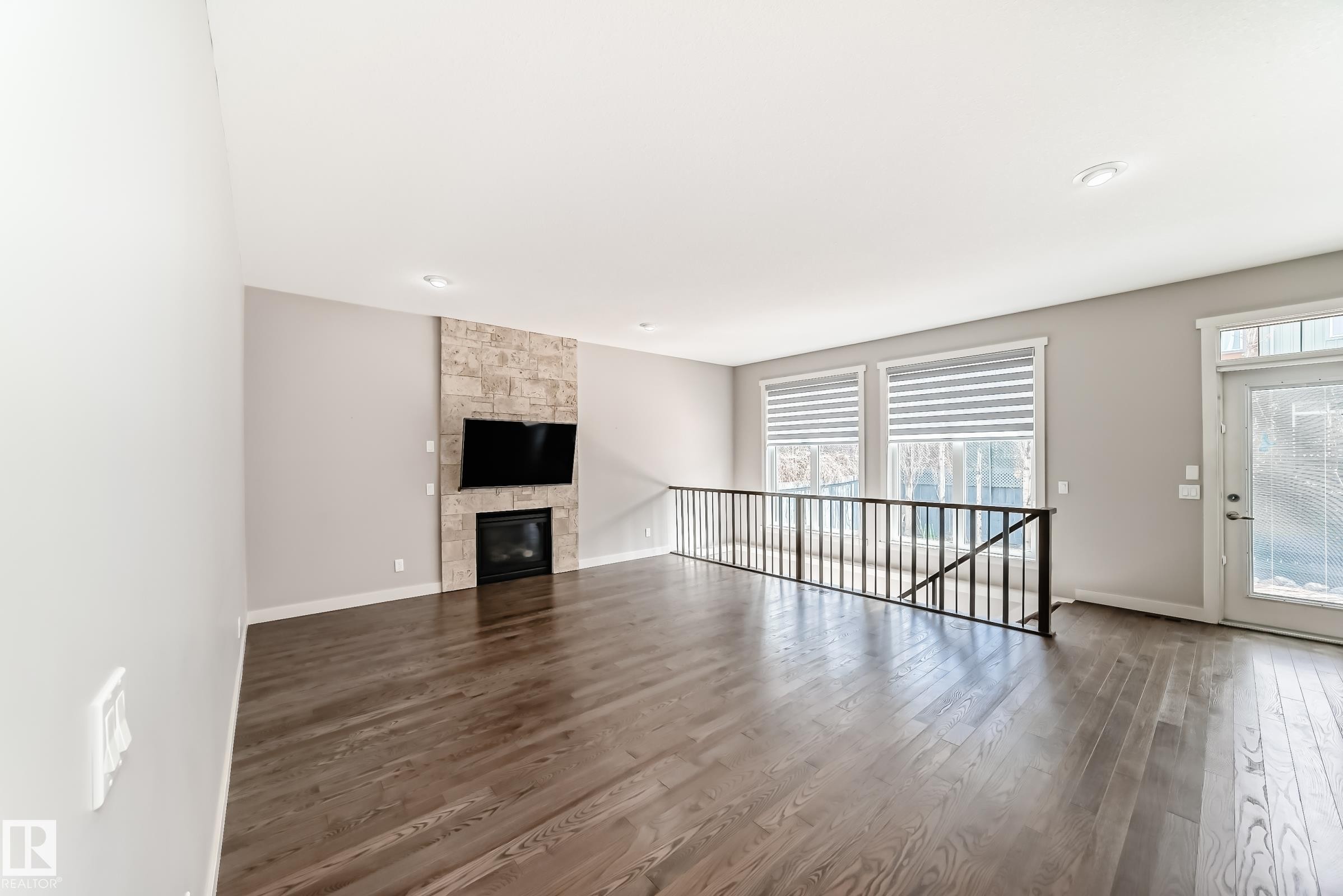 Spacious living area featuring wood-finish flooring, a stone-clad fireplace, and recessed lighting - 7719 Getty Wynd, Edmonton, AB