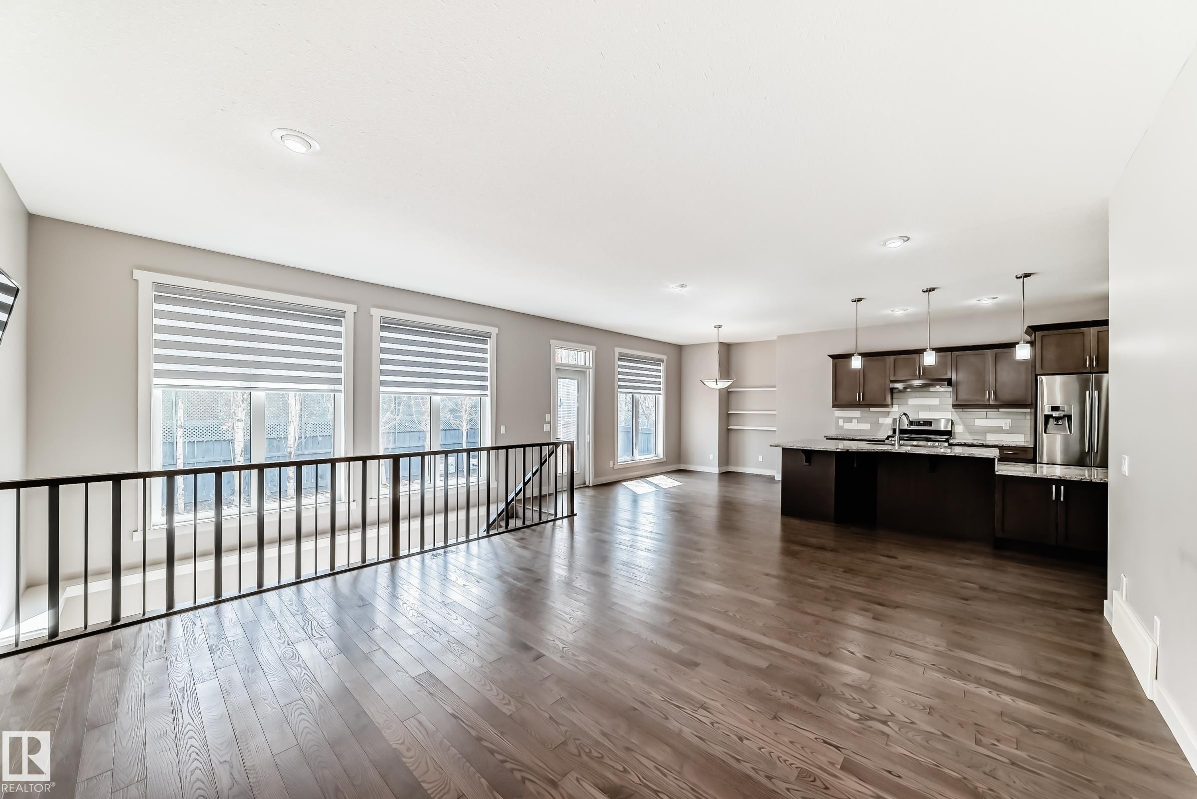 Open-concept main living area with dark wood-finish flooring, recessed lighting, and a modern kitchen - 7719 Getty Wynd, Edmonton, AB