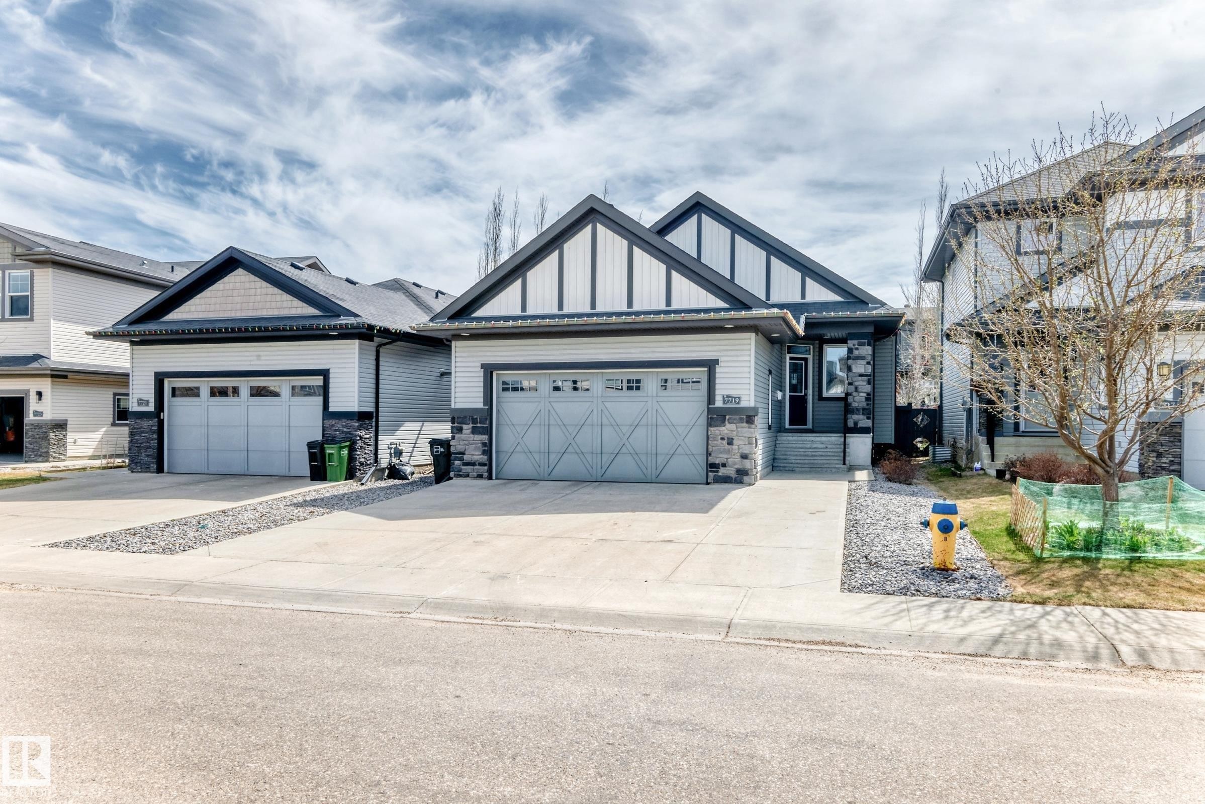 Modern exterior featuring a dark gray roof, light gray siding, and stone accents - 7719 Getty Wynd, Edmonton, AB