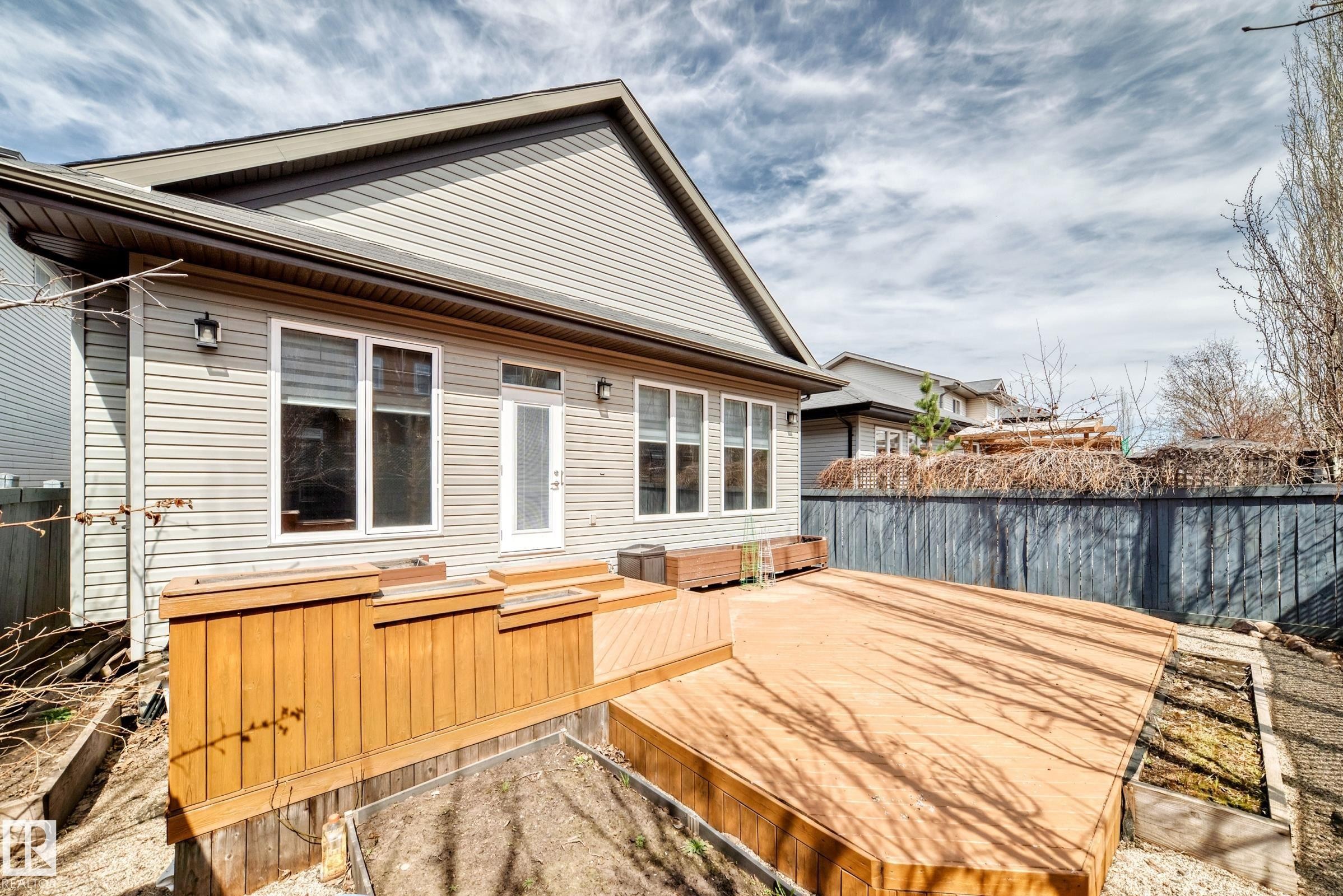 Rear exterior featuring light-toned horizontal siding and a multi-level wood deck - 7719 Getty Wynd, Edmonton, AB