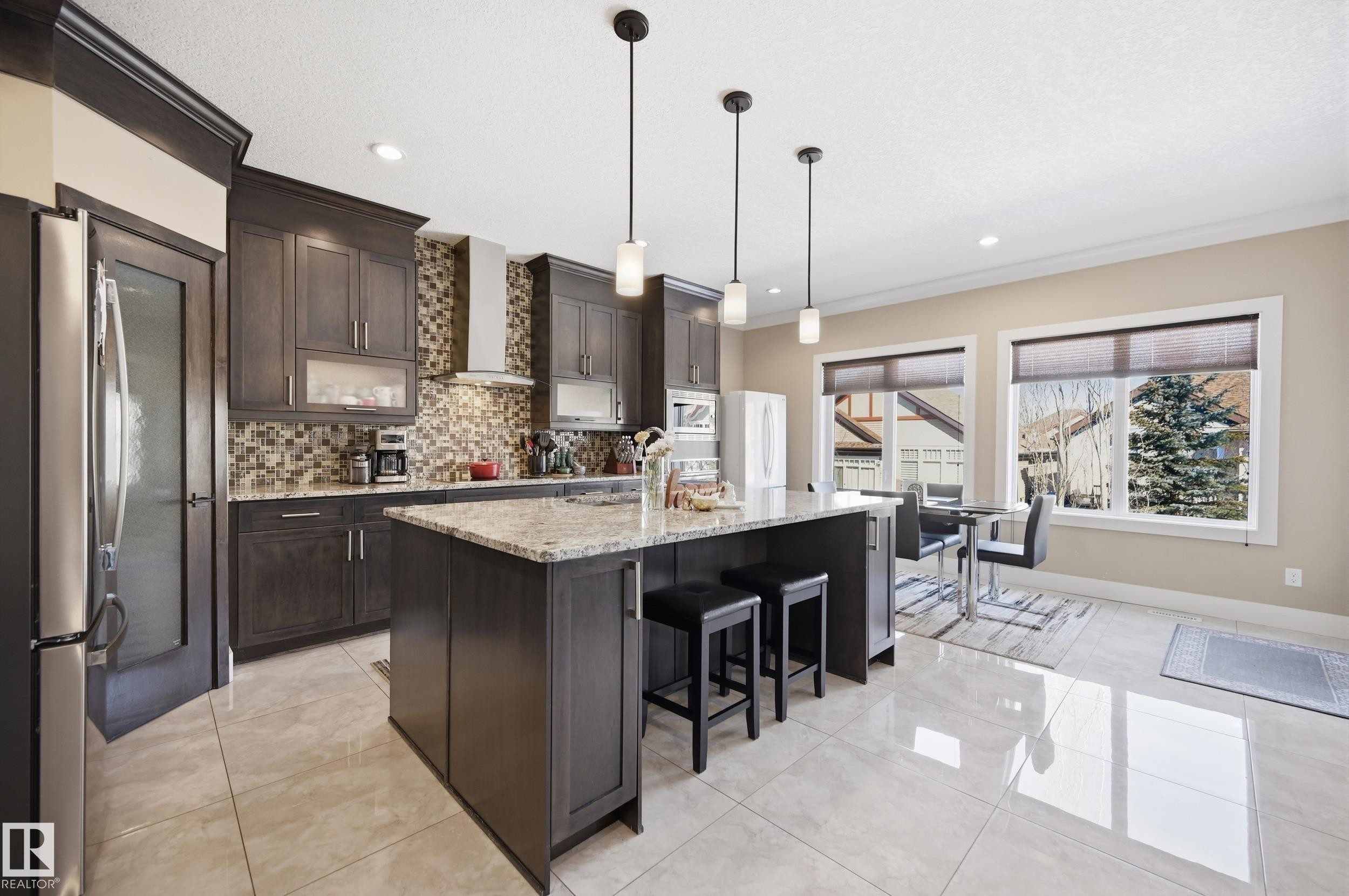 A spacious kitchen featuring dark wood cabinetry, granite countertops, and a tiled backsplash - 2018 Armitage Green, Edmonton, AB - Indoor Photo Showing Kitchen With Upgraded Kitchen