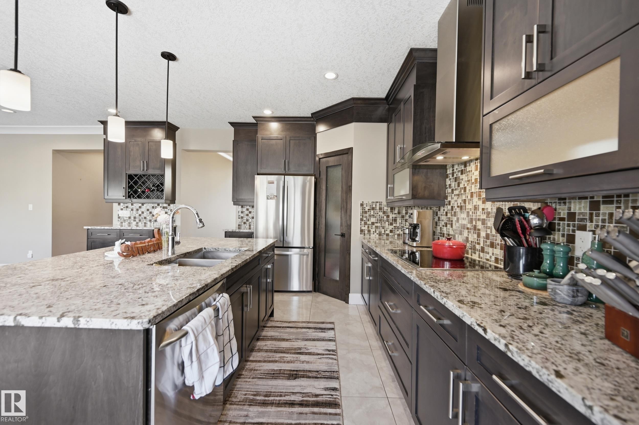 The kitchen features an expansive island with a double sink, granite countertops, and dark cabinetry - 2018 Armitage Green, Edmonton, AB - Indoor Photo Showing Kitchen With Upgraded Kitchen
