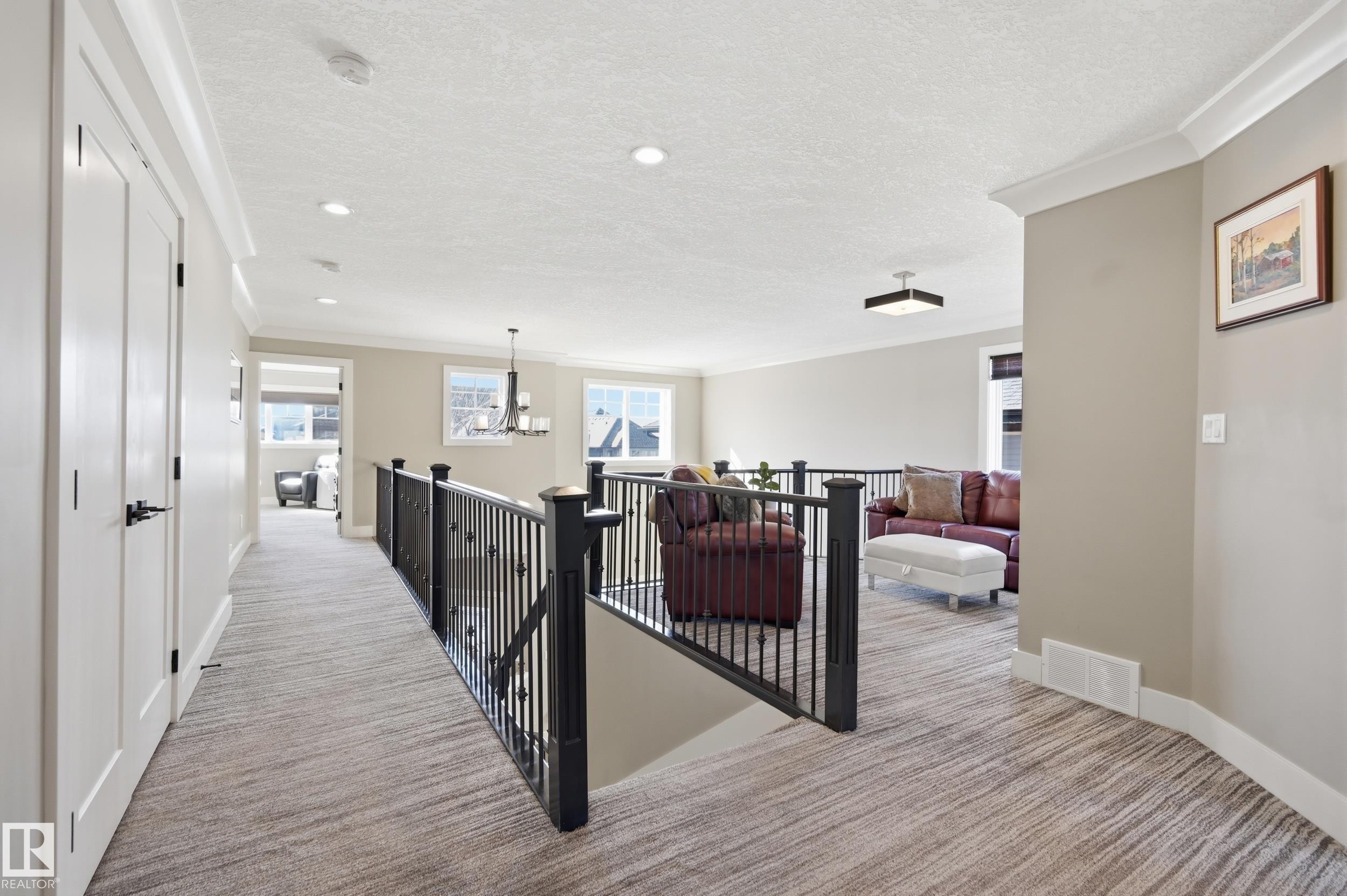 The property features a hallway with light-colored walls and a patterned carpet, leading to an open area visible through a black metal railing - 2018 Armitage Green, Edmonton, AB - Indoor Photo Showing Other Room