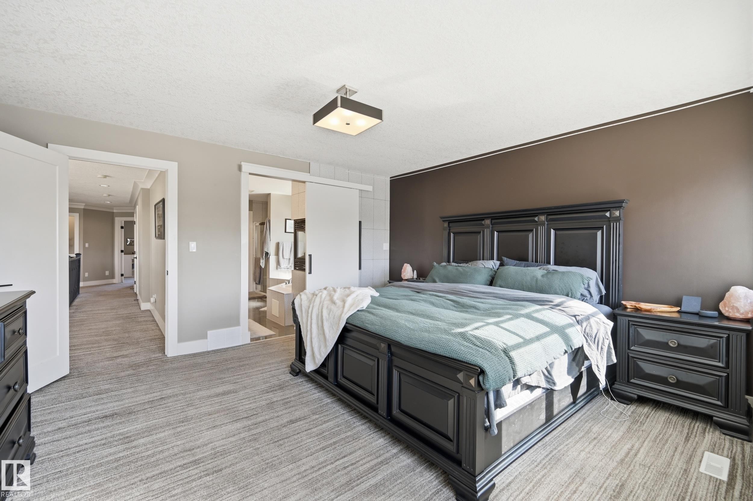 This bedroom features a dark wooden bed frame and matching nightstands, a neutral-toned accent wall, and light-colored carpeting - 2018 Armitage Green, Edmonton, AB - Indoor Photo Showing Bedroom