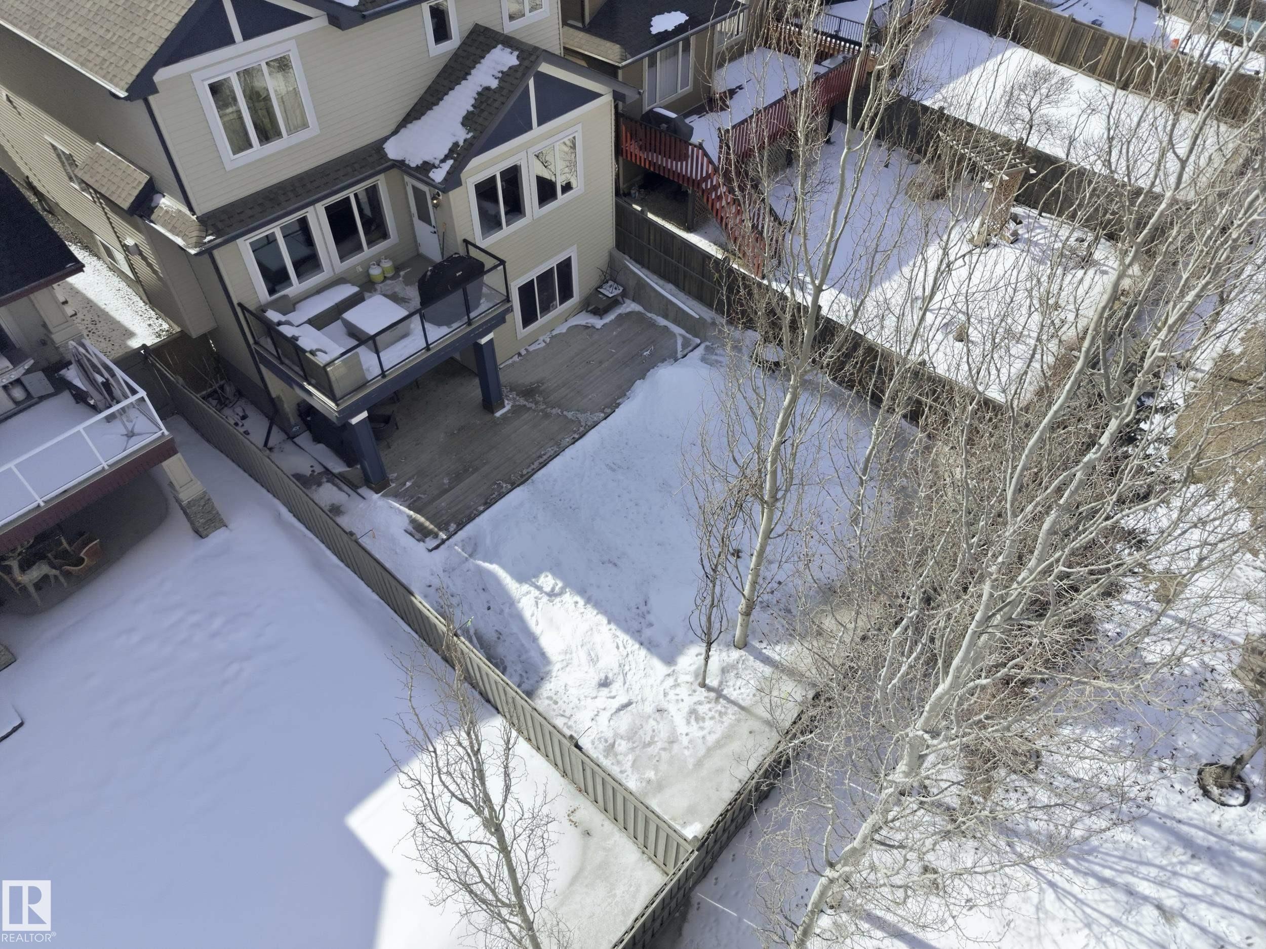 The property features a two-story exterior with light-colored siding and a dark roof, a raised deck with a glass railing, and a fenced yard - 2018 Armitage Green, Edmonton, AB - Outdoor