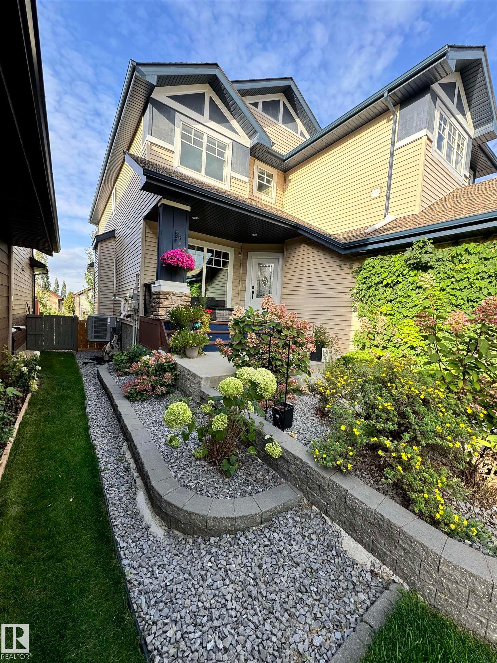 The property exterior features two stories, a front entrance with a decorative glass door, and a landscaped front yard with a gravel path, lawn, and various plantings - 2018 Armitage Green, Edmonton, AB - Outdoor