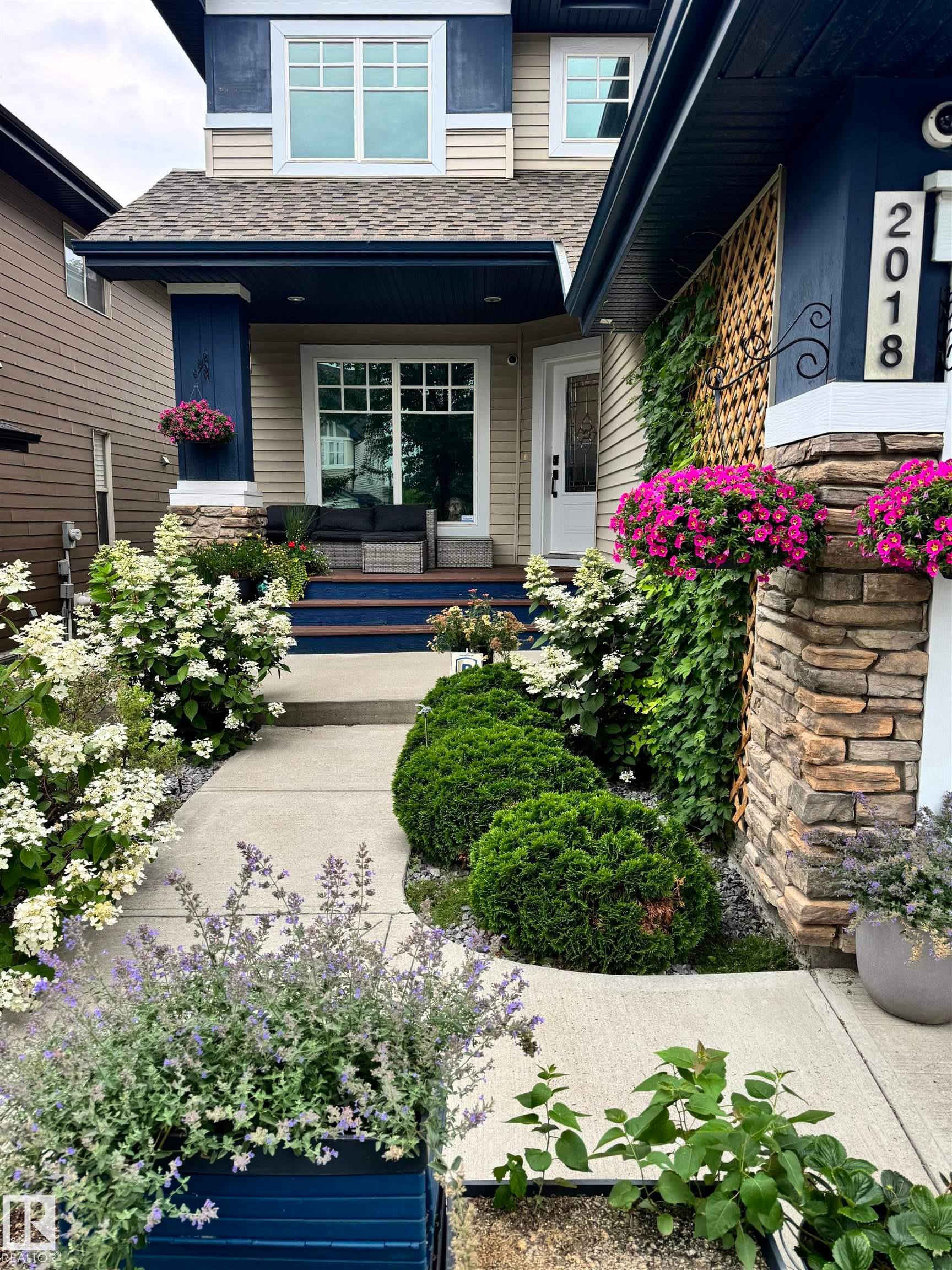 The property features a welcoming entrance with a stone-clad pillar, a light-colored exterior siding, and a contrasting dark blue trim - 2018 Armitage Green, Edmonton, AB - Outdoor With Deck Patio Veranda