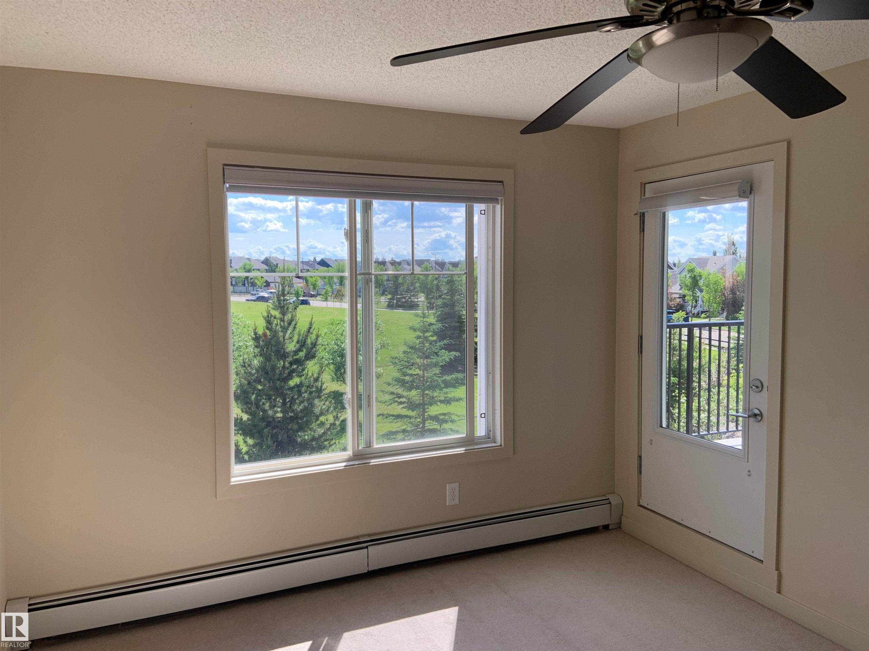 Interior space featuring a window with expansive outdoor views, a glass-paneled door opening to a balcony, a ceiling fan with integrated lighting, and baseboard heating - 307 6084 Stanton Drive, Edmonton, AB - Indoor Photo Showing Other Room