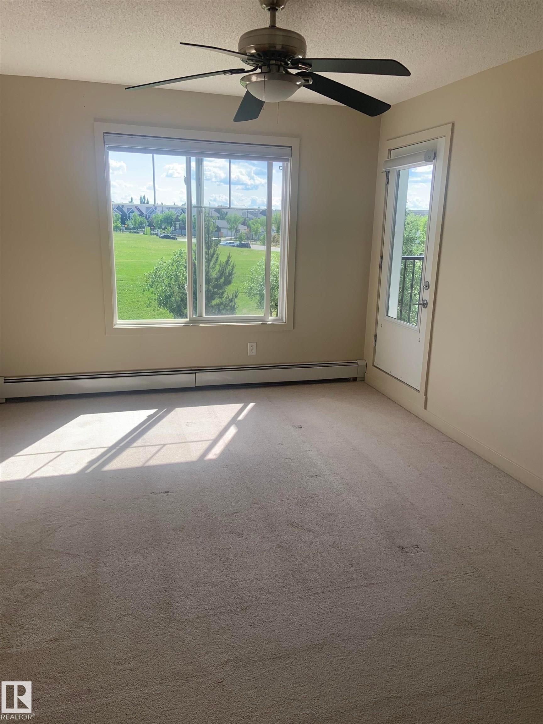 Bright room featuring a large window, a ceiling fan with light fixture, a baseboard heater, and a door with a small balcony - 307 6084 Stanton Drive, Edmonton, AB - Indoor Photo Showing Other Room