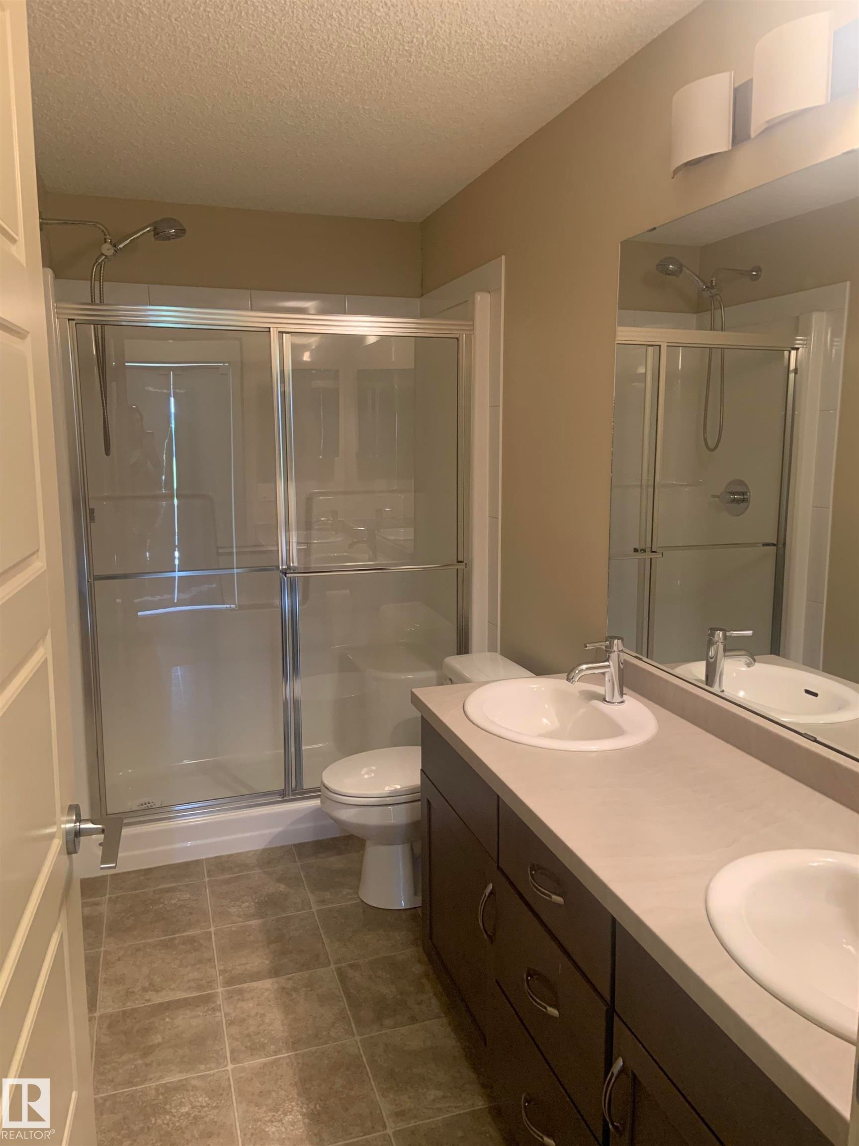 Bathroom featuring a dual vanity with undermount sinks, a light-toned countertop, and dark wood-finish cabinetry - 307 6084 Stanton Drive, Edmonton, AB - Indoor Photo Showing Bathroom