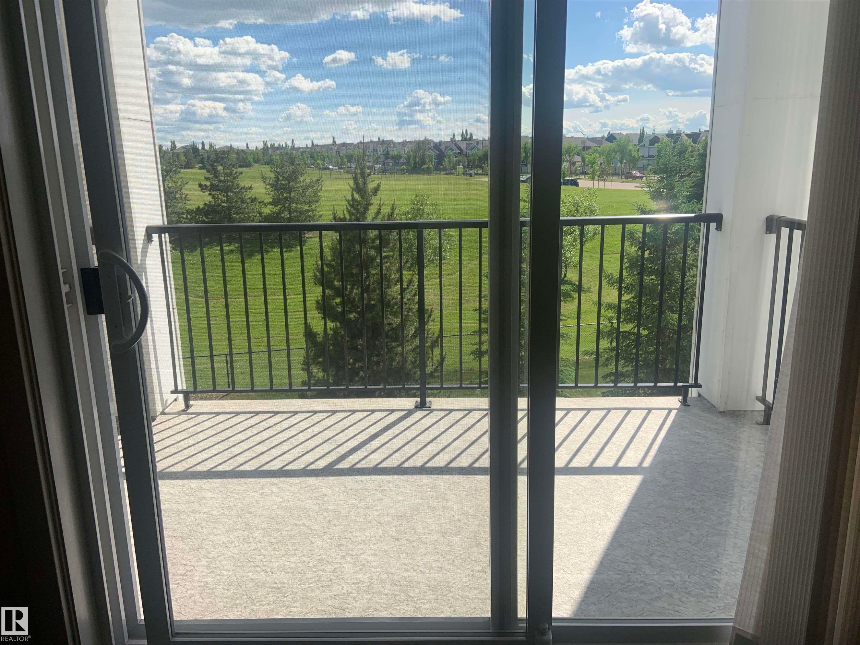 Balcony featuring a black metal railing and concrete flooring, overlooking a green expanse with mature trees - 307 6084 Stanton Drive, Edmonton, AB - With Balcony With View