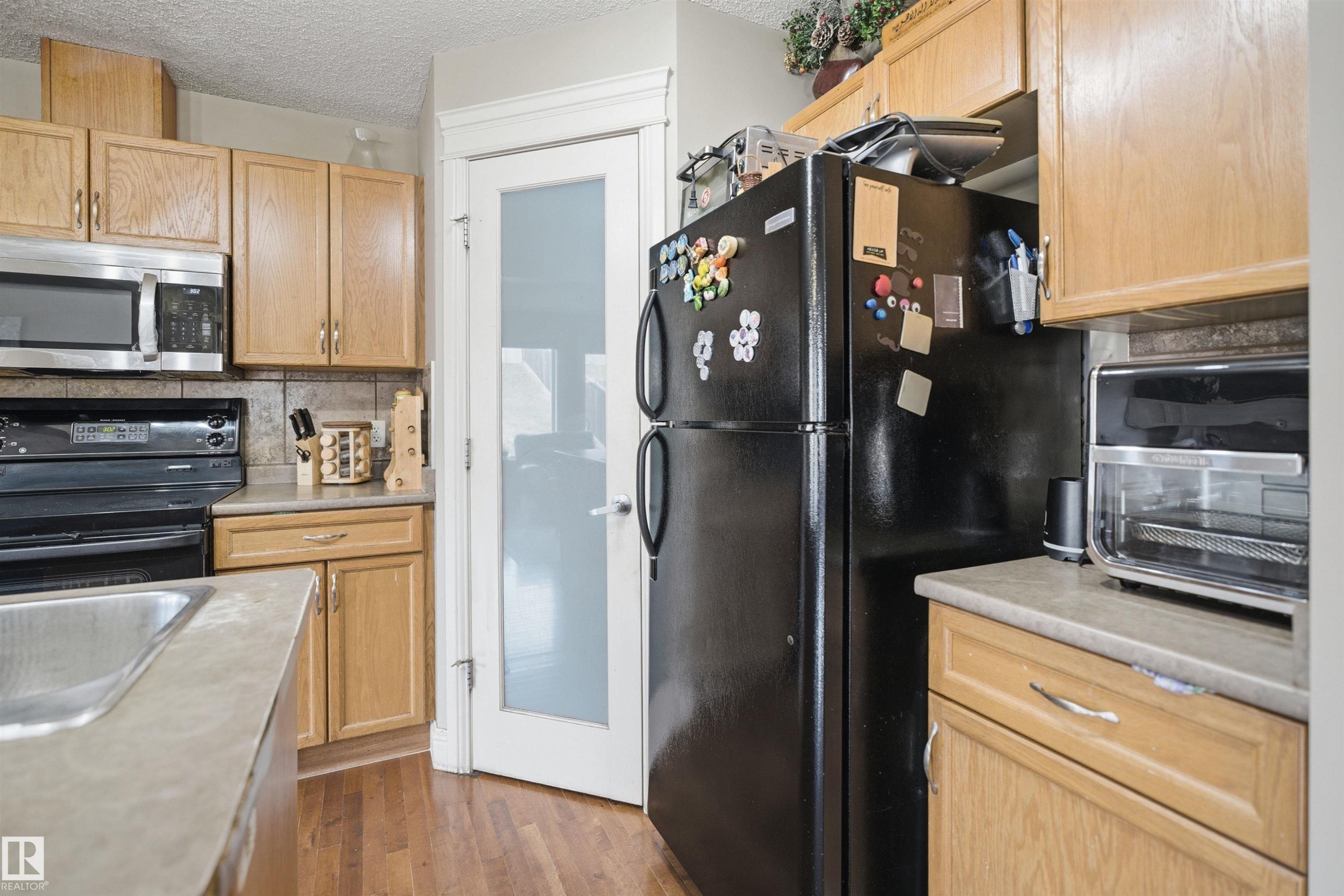 Kitchen featuring wood-finish cabinetry, stainless steel microwave, black electric range, and wood-finish flooring - 3533 11 Street, Edmonton, AB