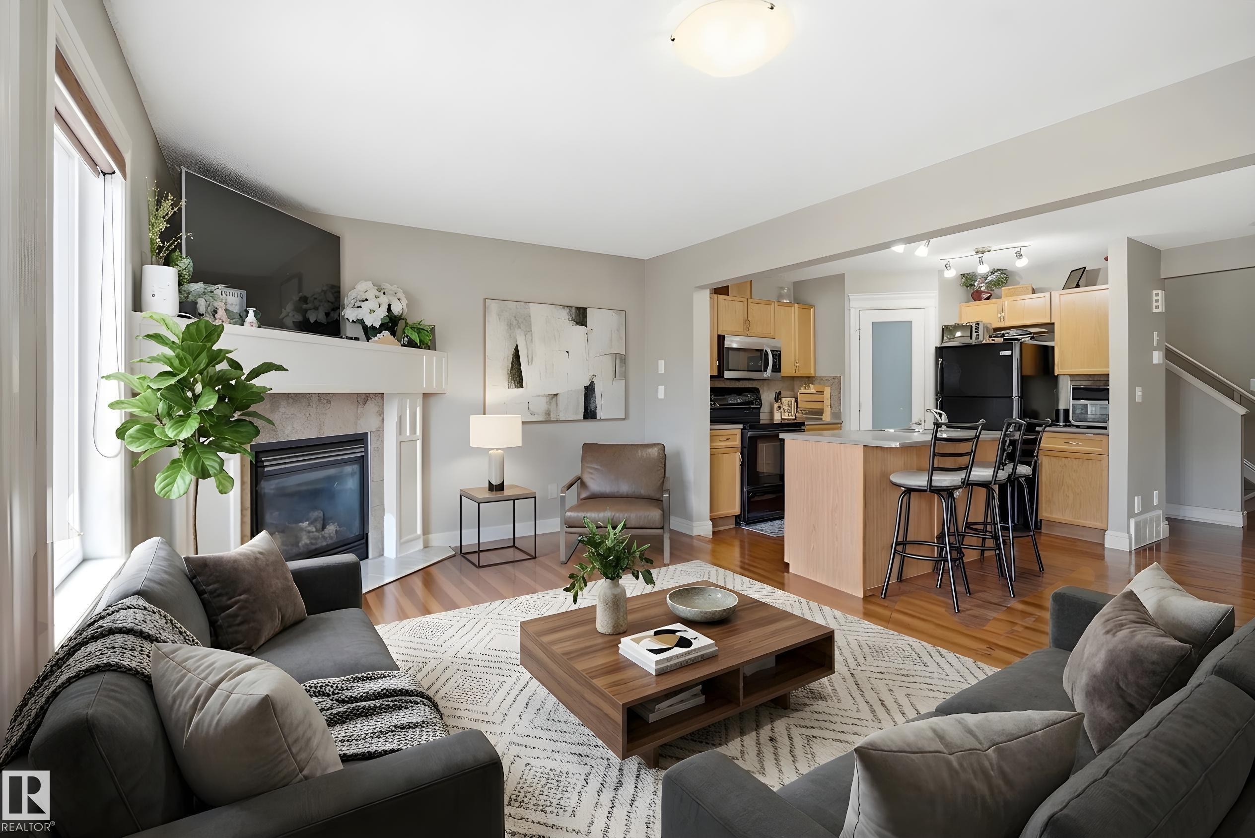 Open-concept living space featuring a fireplace with a stone surround and a white mantel, hardwood flooring, and a kitchen with light wood cabinetry and a central island - 3533 11 Street, Edmonton, AB