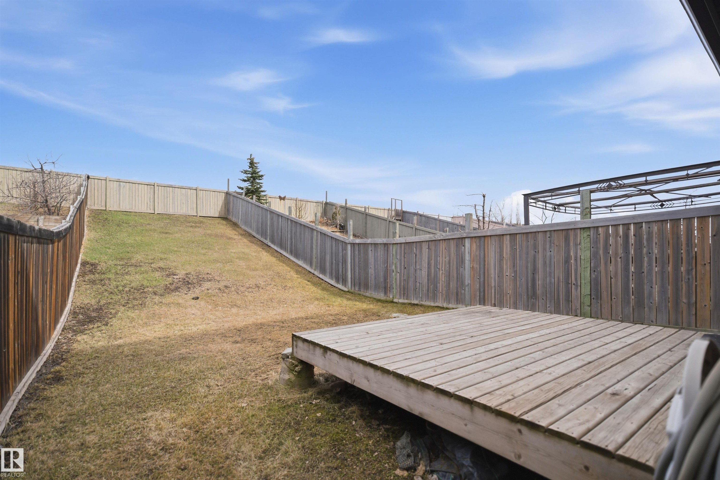 Expansive backyard featuring a wood deck, sloped lawn, and perimeter wood fencing - 3533 11 Street, Edmonton, AB