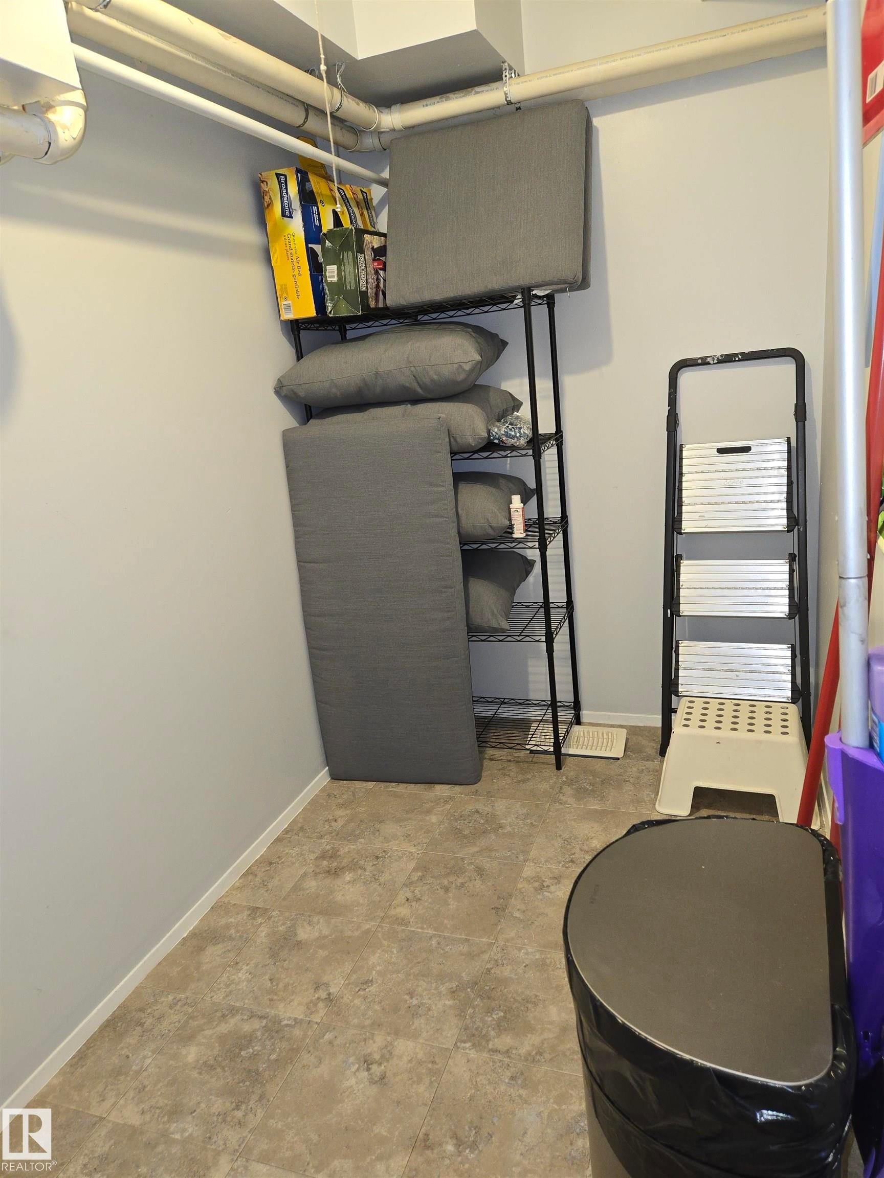 Utility space featuring light gray walls, an exposed ceiling with white piping, and neutral-toned square tile flooring - 202 24 Alpine Place, St. Albert, AB - Indoor