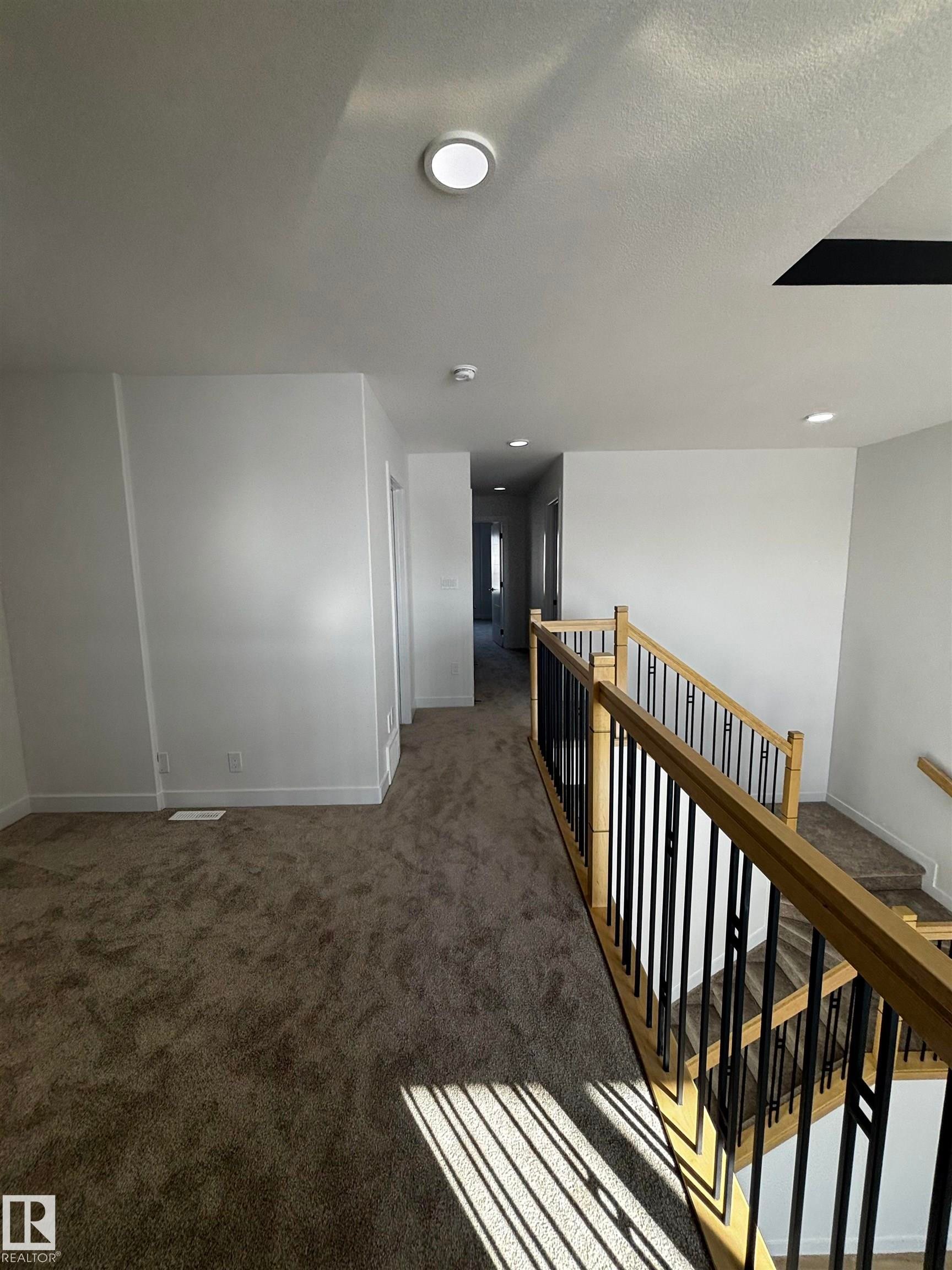 The property features a staircase with light wood railings and black vertical spindles, leading down to carpeted steps - 2012 210 St, Edmonton, AB - Indoor Photo Showing Other Room