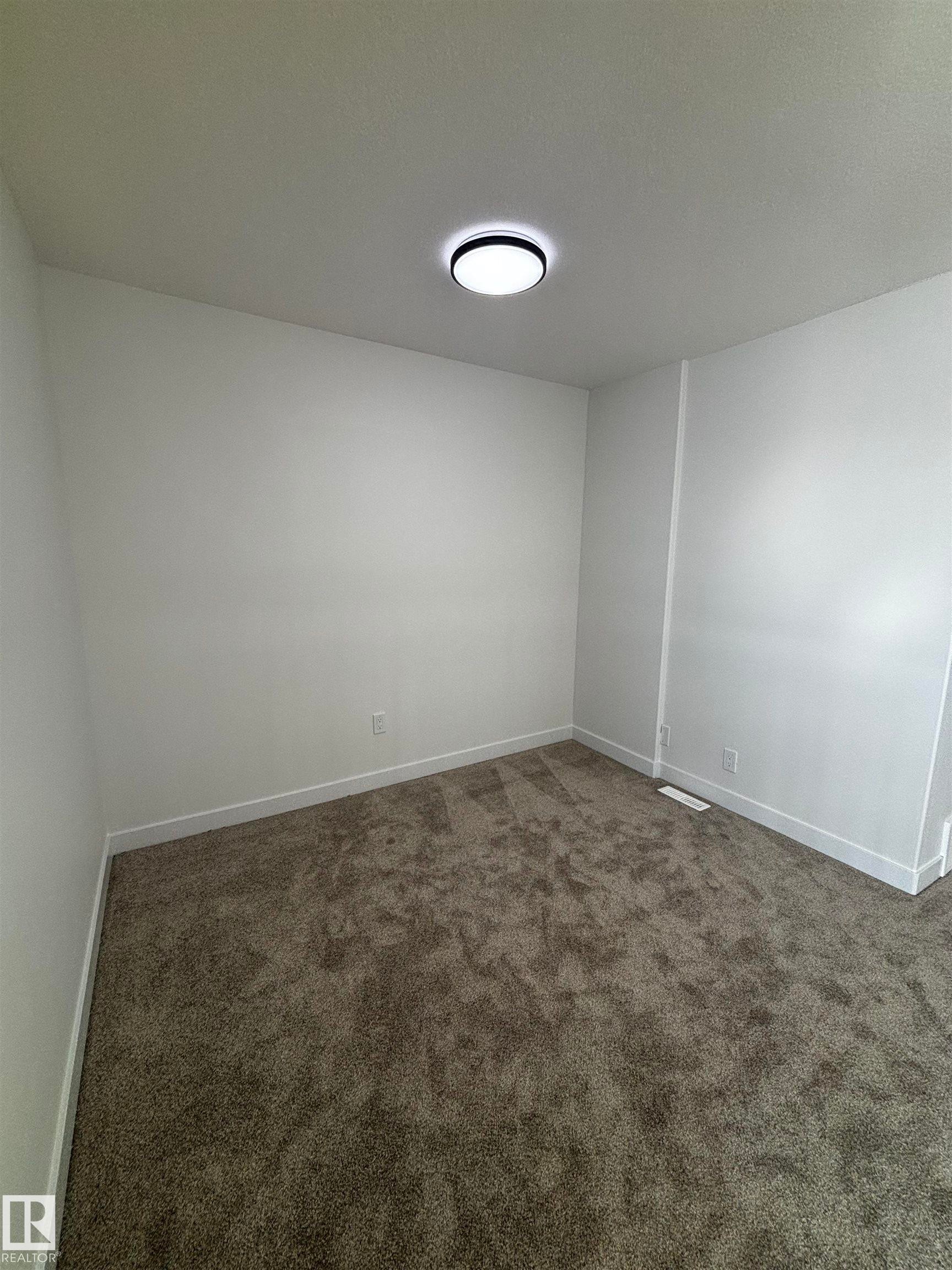 This room features plush grey carpeting, white walls, white baseboards, and a modern circular ceiling light fixture - 2012 210 St, Edmonton, AB - Indoor Photo Showing Other Room