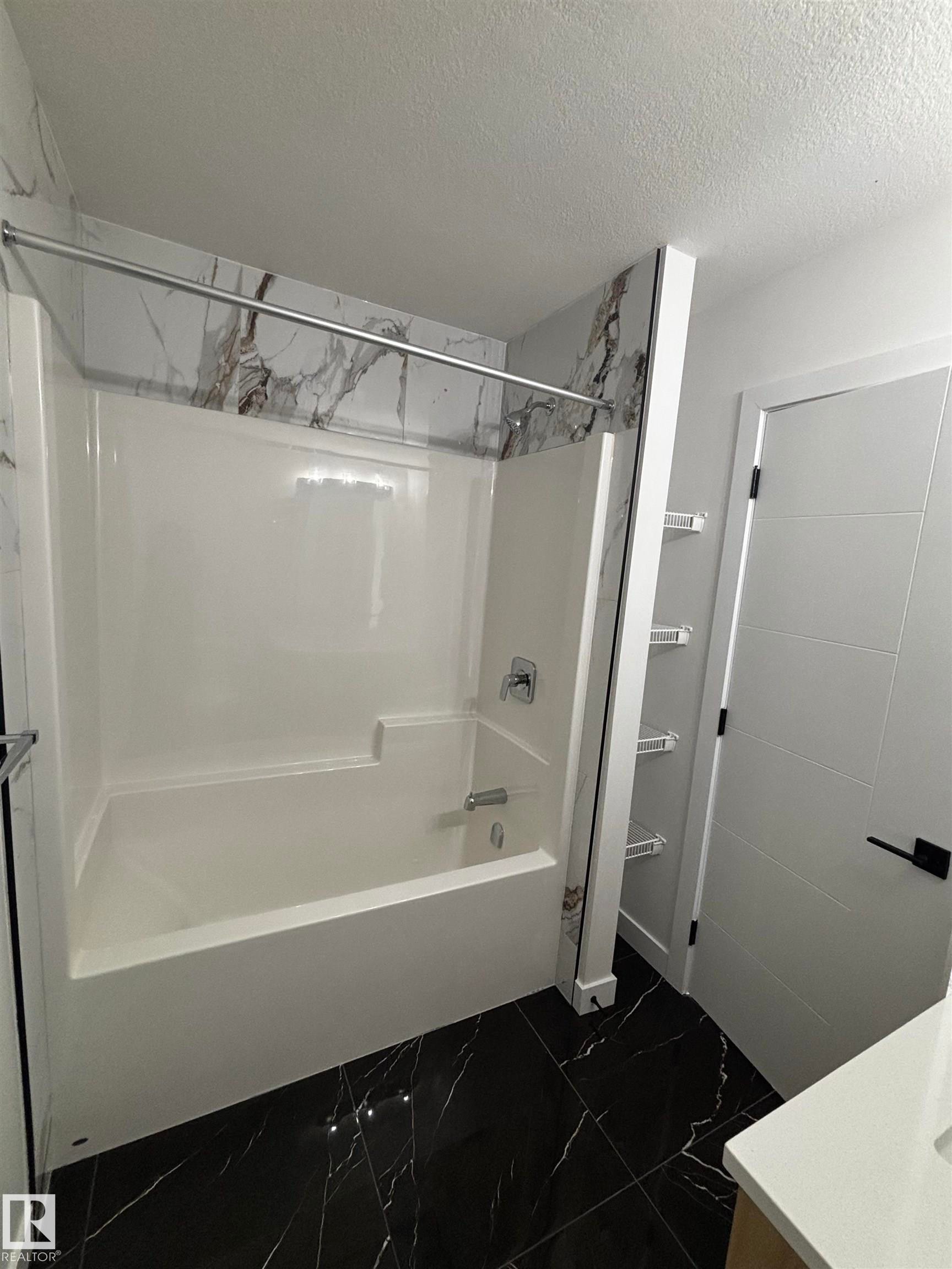 Bathroom featuring a white tub and shower combination with a modern shower head and fixture, dark marble-style tile flooring, and a white interior door with a black handle - 2012 210 St, Edmonton, AB - Indoor Photo Showing Bathroom