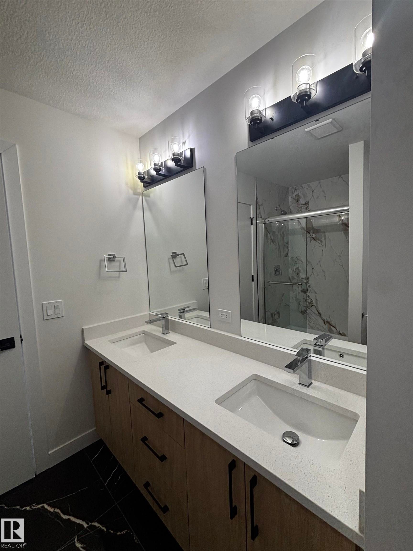 Bathroom featuring a double vanity with a light-colored countertop and wooden cabinetry, two rectangular mirrors, and black tiled flooring - 2012 210 St, Edmonton, AB - Indoor Photo Showing Bathroom