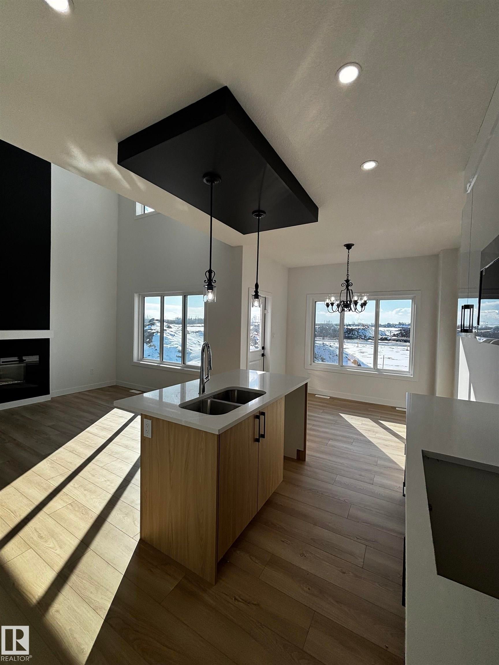 The open-concept living area features light wood-style flooring, an island with a double sink and light-colored countertop, and a black ceiling accent with pendant lights - 2012 210 St, Edmonton, AB - Indoor