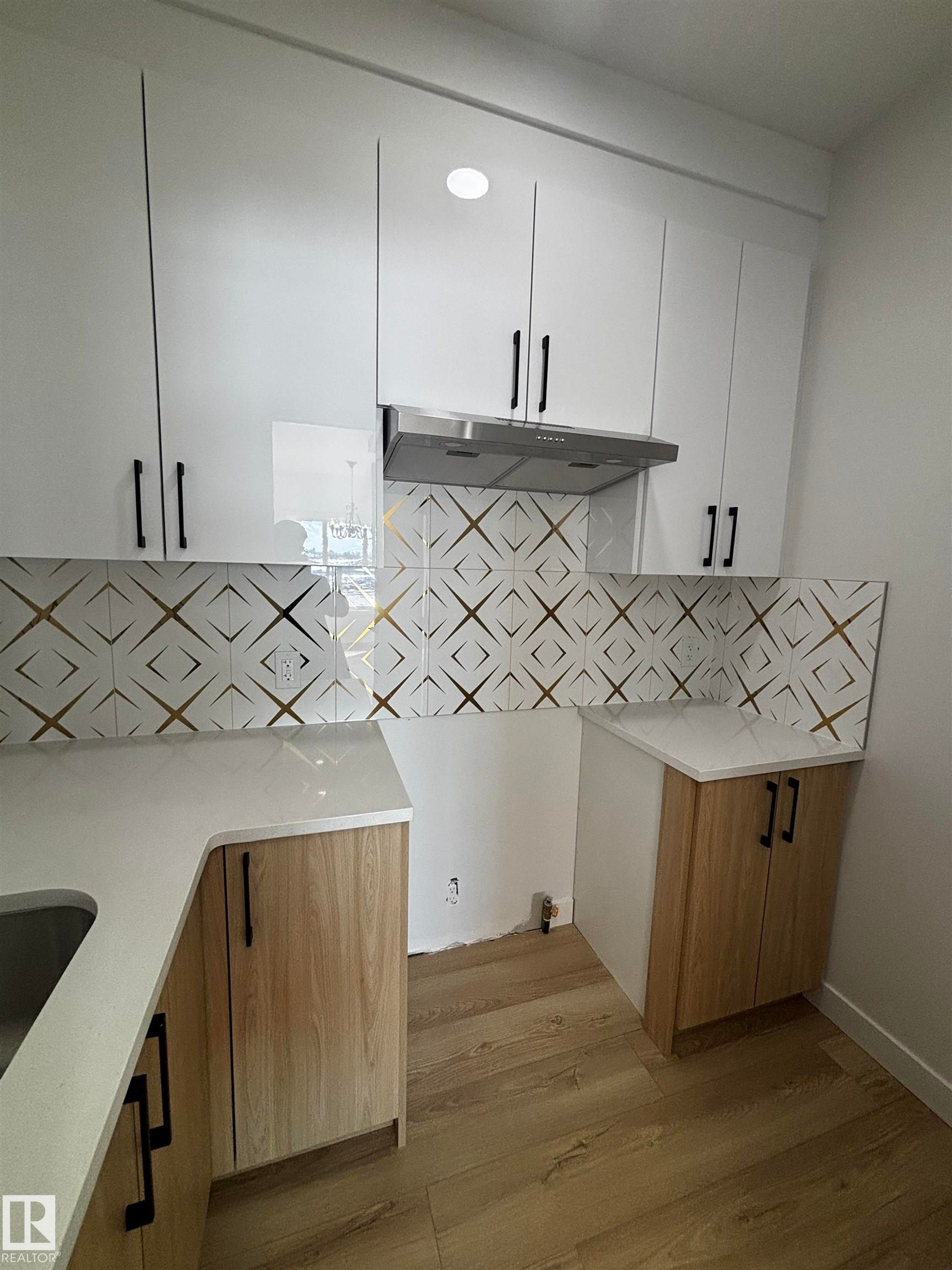 The kitchen features white upper cabinetry with black handles, a patterned backsplash, and light wood-look lower cabinetry - 2012 210 St, Edmonton, AB - Indoor
