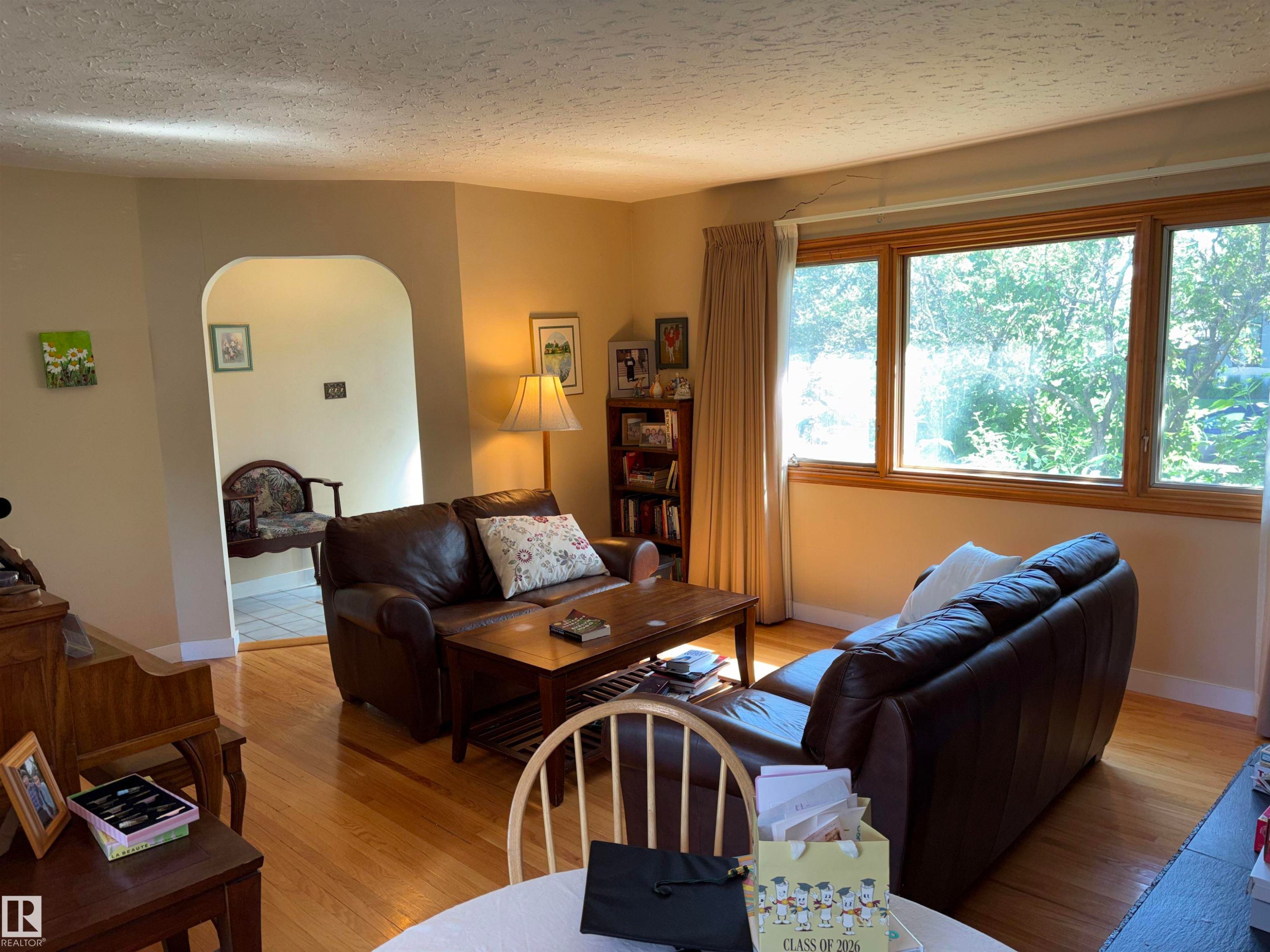 Hardwood flooring spans this living area, featuring an arched doorway and a large picture window with wood trim - 8812 146 Street, Edmonton, AB