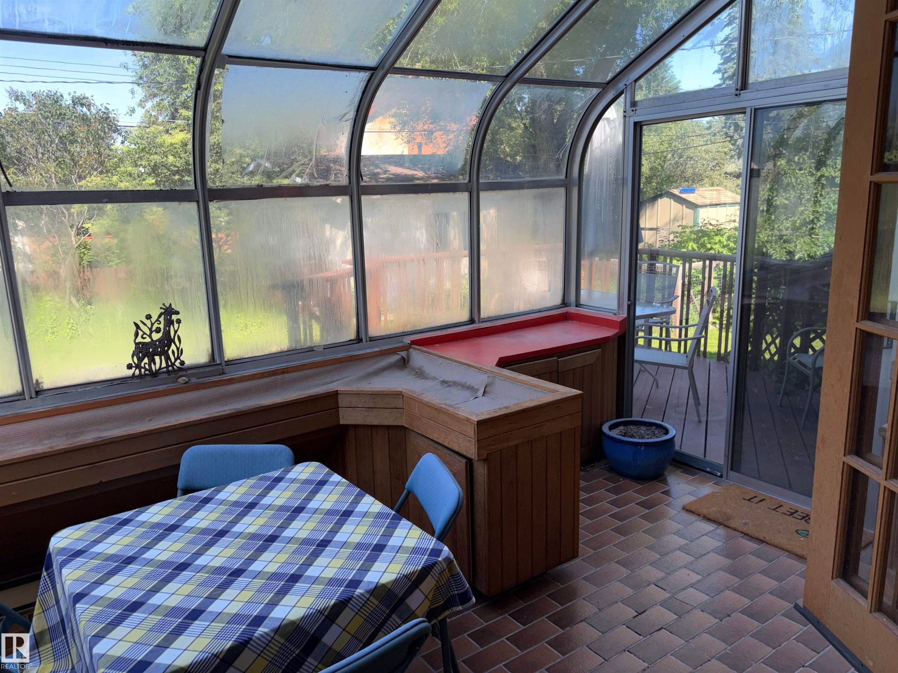 Sunroom featuring a curved glass roof, brick-patterned flooring, built-in wooden cabinetry, a built-in planter with a red countertop, and direct access to an outdoor deck - 8812 146 Street, Edmonton, AB