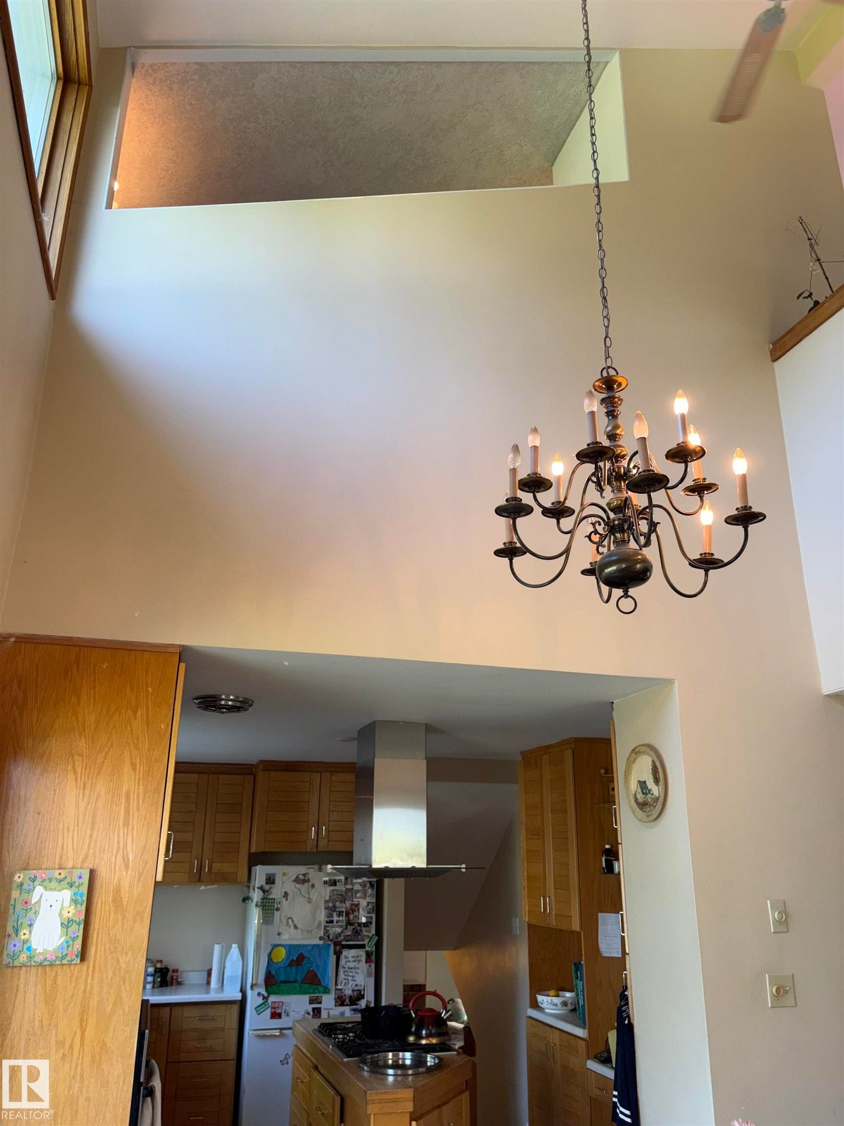 Vaulted ceiling featuring a multi-arm chandelier, an upper-level window, and an exposed ceiling fan - 8812 146 Street, Edmonton, AB