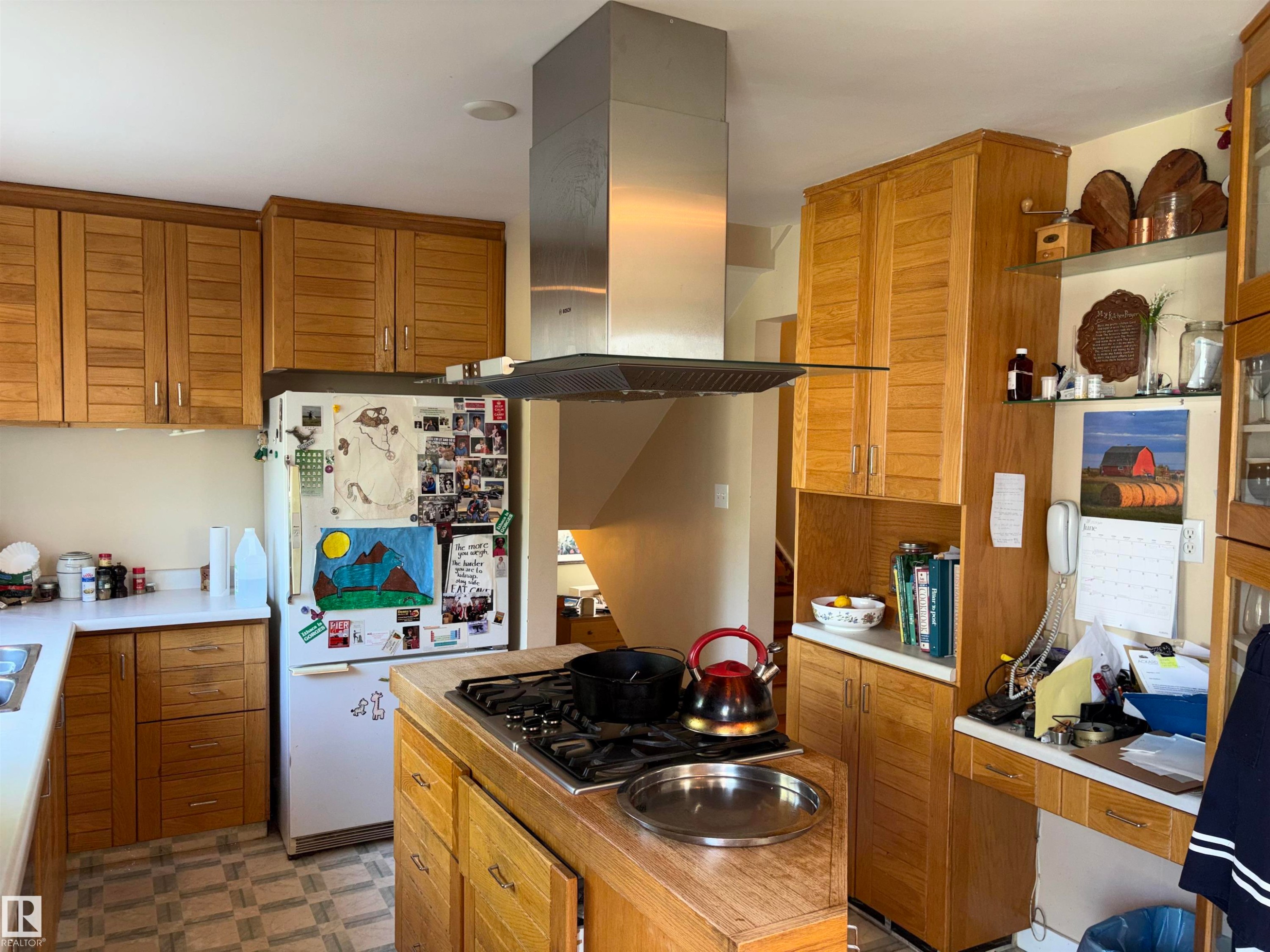 Kitchen featuring wood cabinetry, white countertops, a stainless steel range hood, and a gas cooktop on a central island - 8812 146 Street, Edmonton, AB