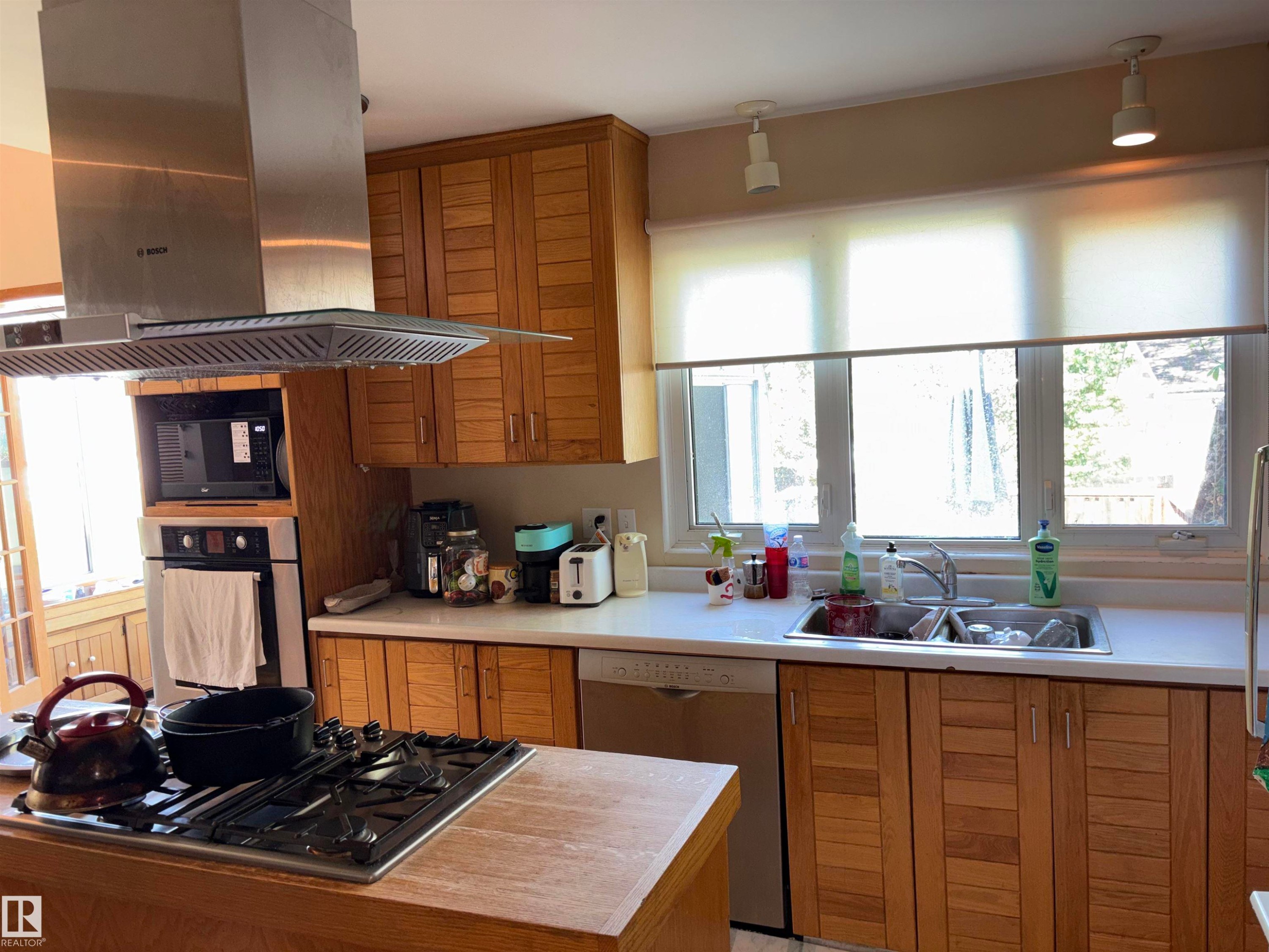 Modern kitchen featuring natural wood cabinetry, stainless steel appliances, a gas cooktop, and a double basin sink - 8812 146 Street, Edmonton, AB