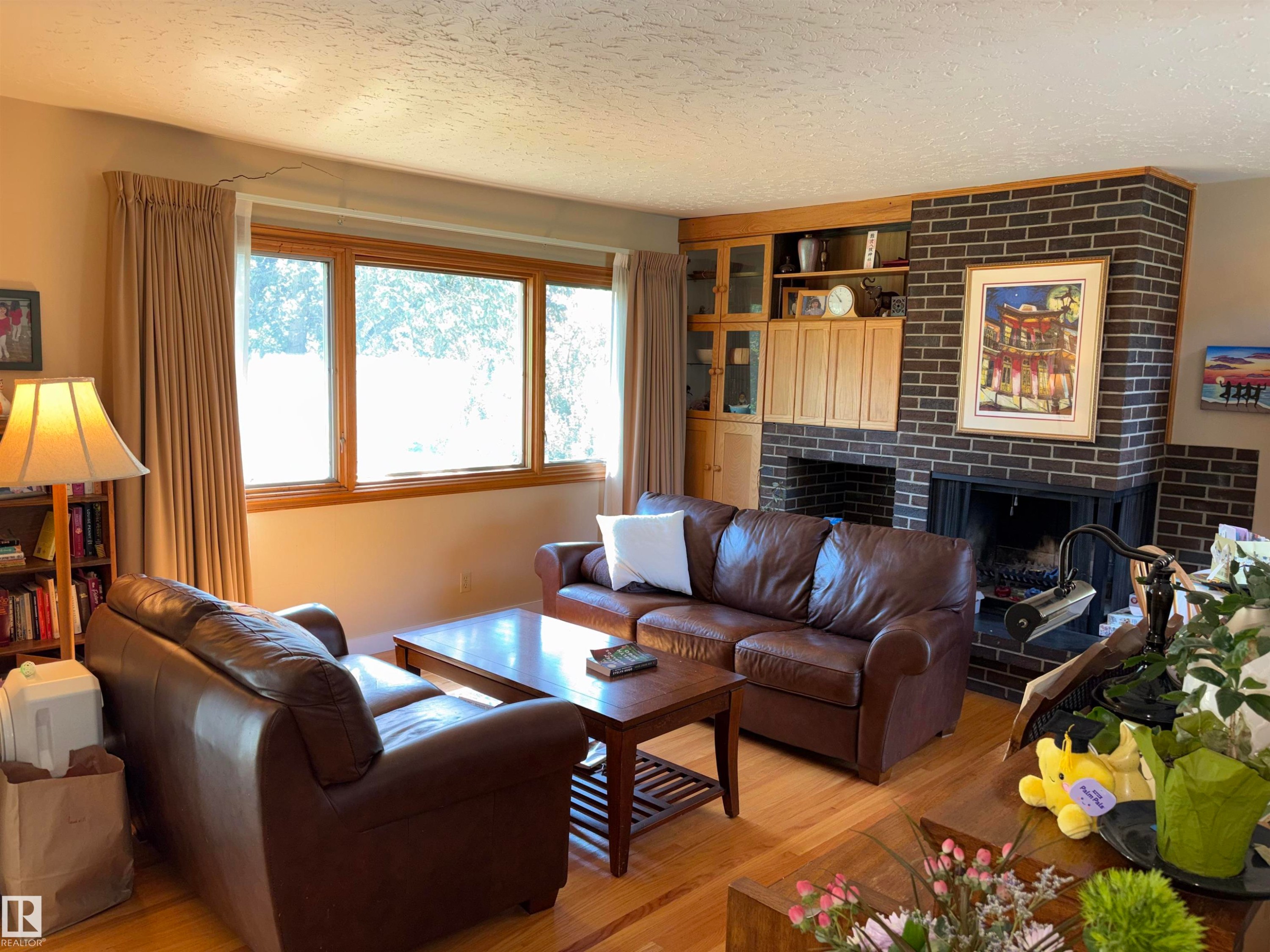 Hardwood flooring throughout featuring a brick fireplace with a built-in wood mantel and cabinetry - 8812 146 Street, Edmonton, AB
